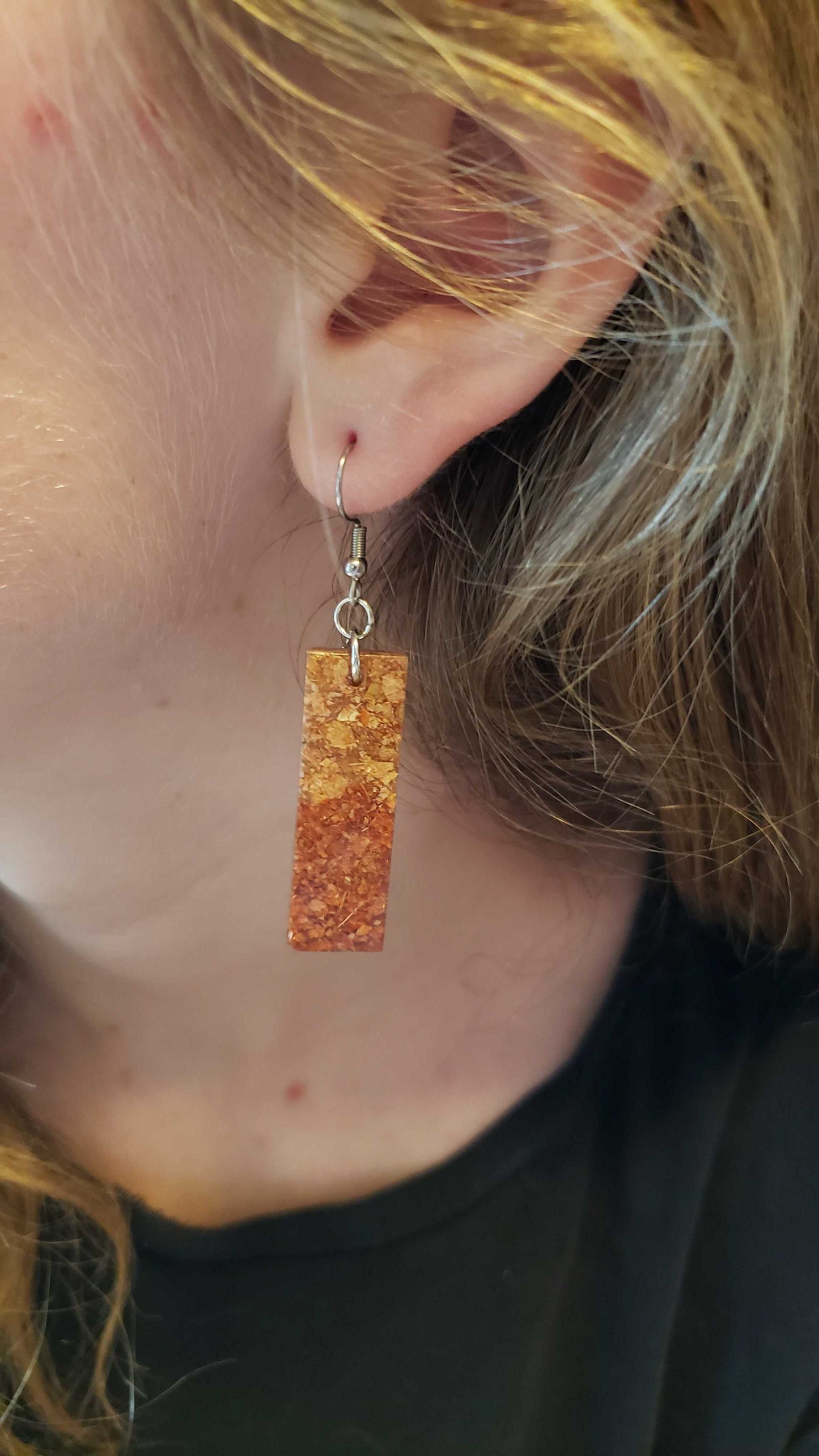 Close-up of a person wearing a gold autumn inspired rectangular earring made of dried leaves.