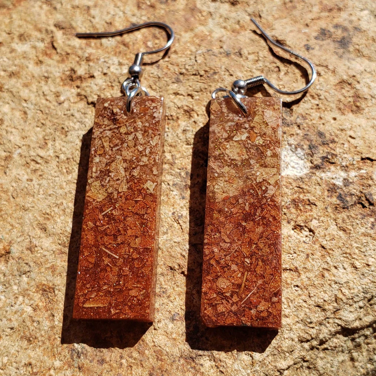 Pair of rectangular dried leaf earrings on a textured brown surface