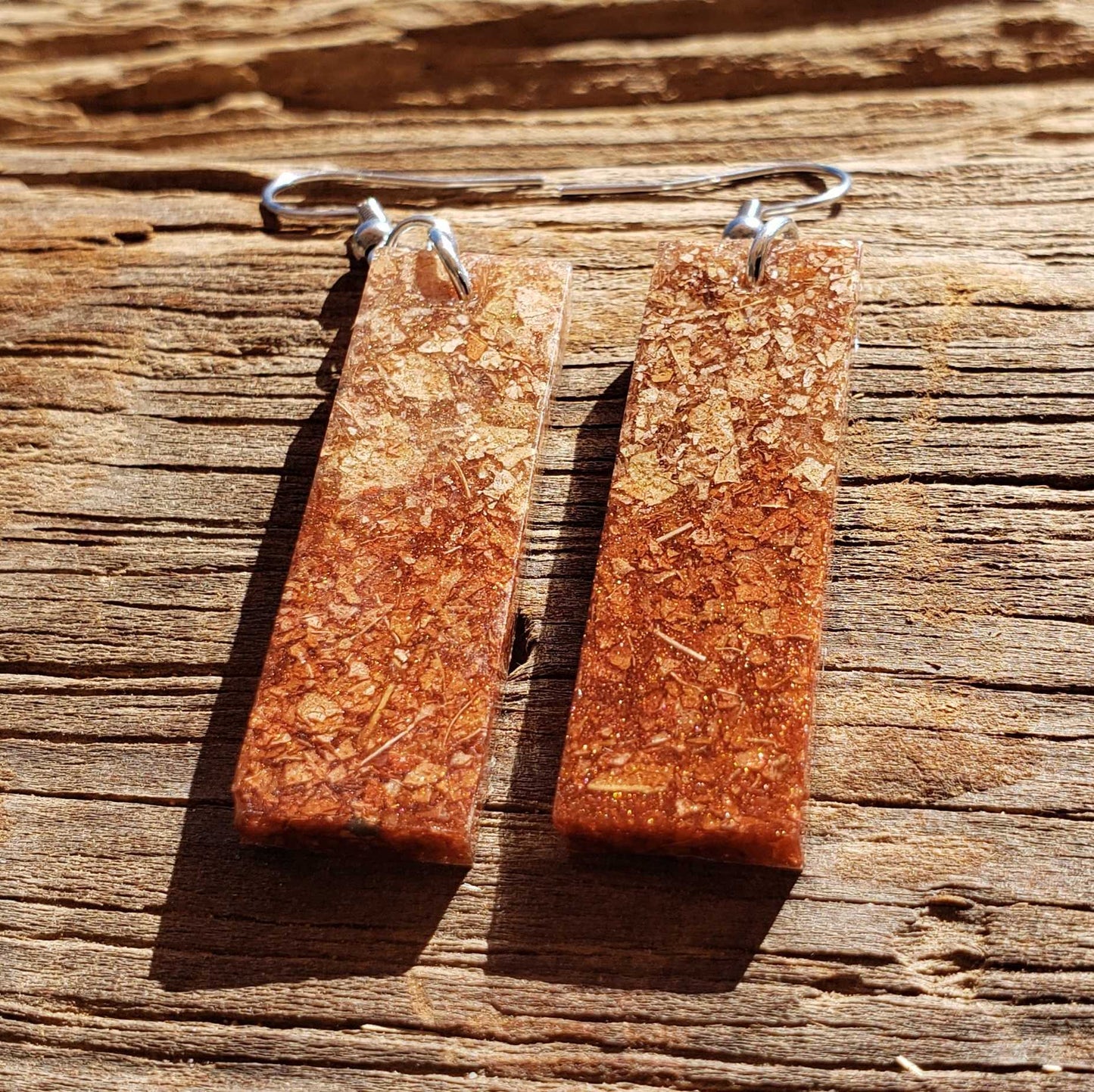 Pair of rectangular brown earrings made from dried leaves on a wooden surface