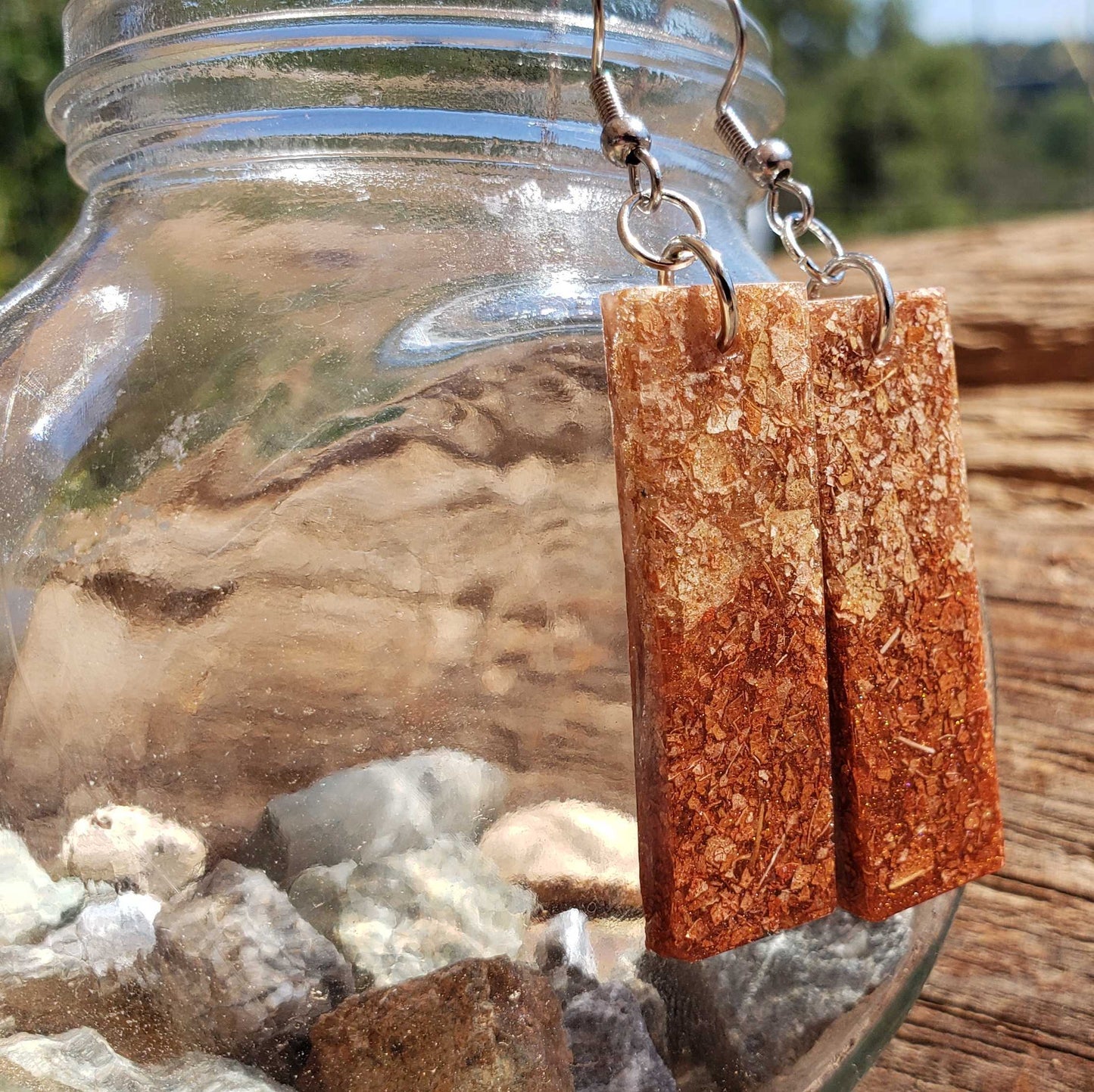 Dried leaf earrings hanging from a glass jar with a natural background
