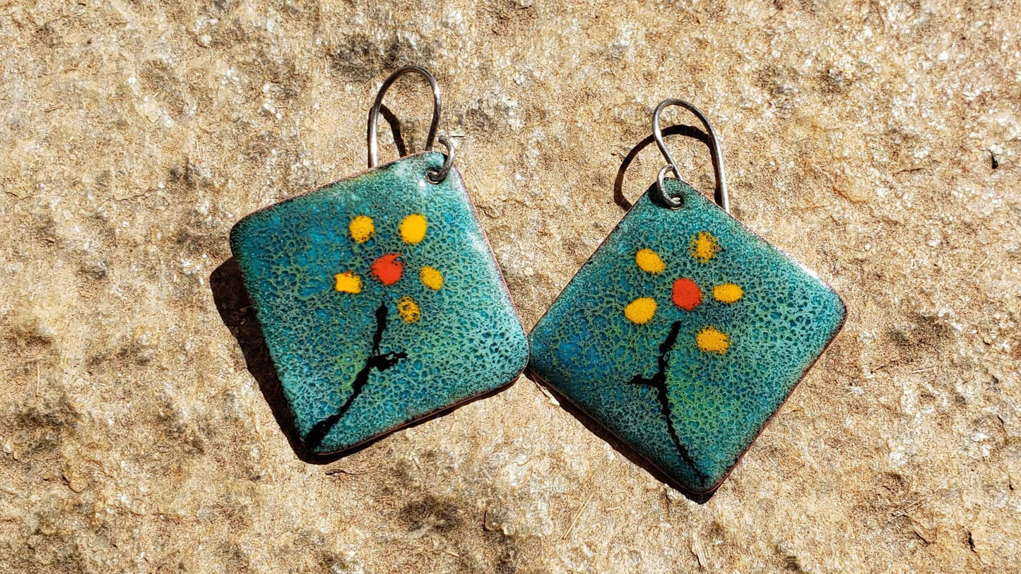 Pair of turquoise square earrings with floral design on a stone surface