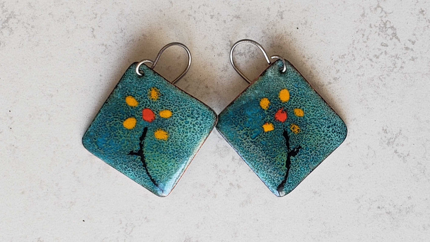 Pair of square copper earrings with blue and orange design on a light gray background