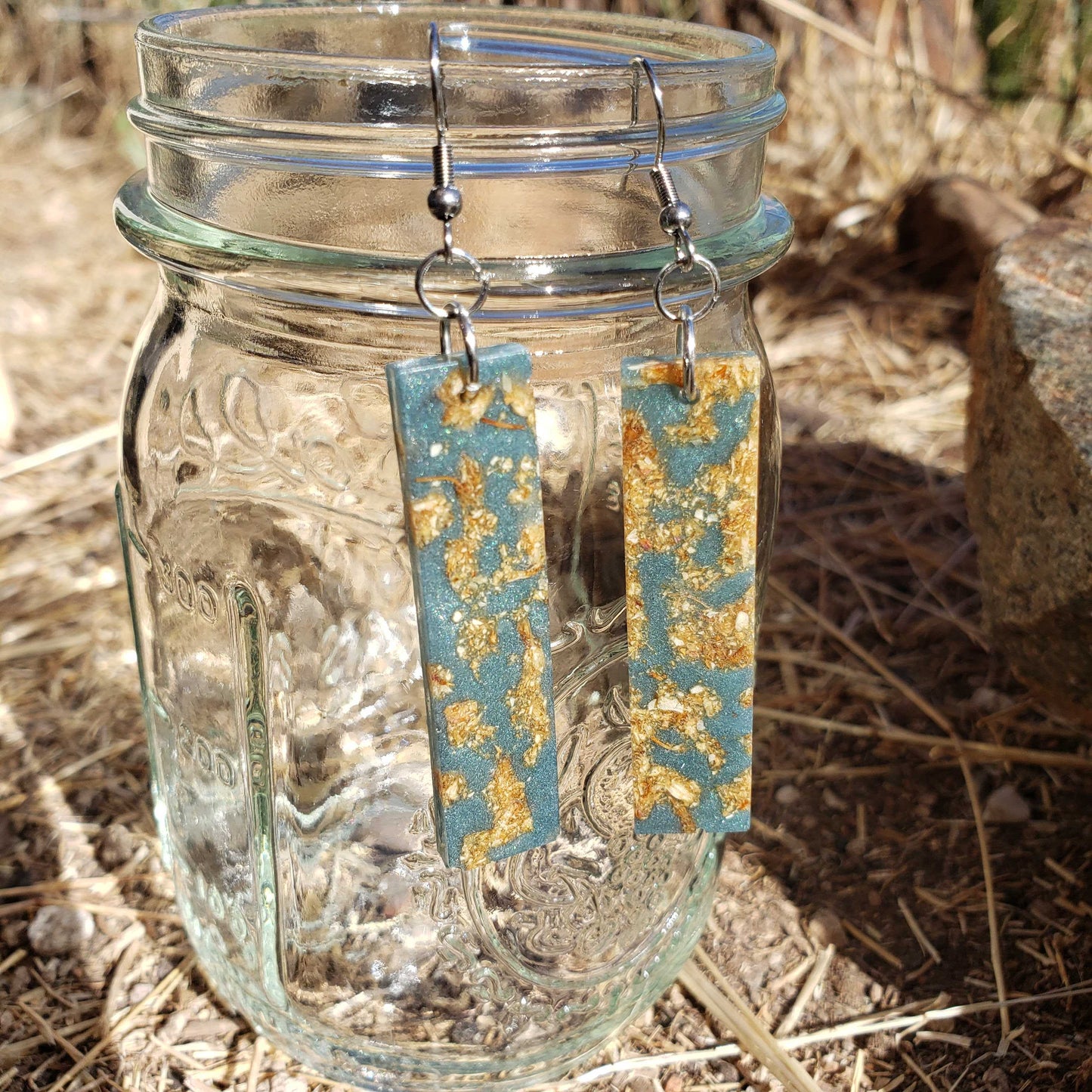 Pair of earrings with blue and gold design hanging from a glass jar on a natural background.