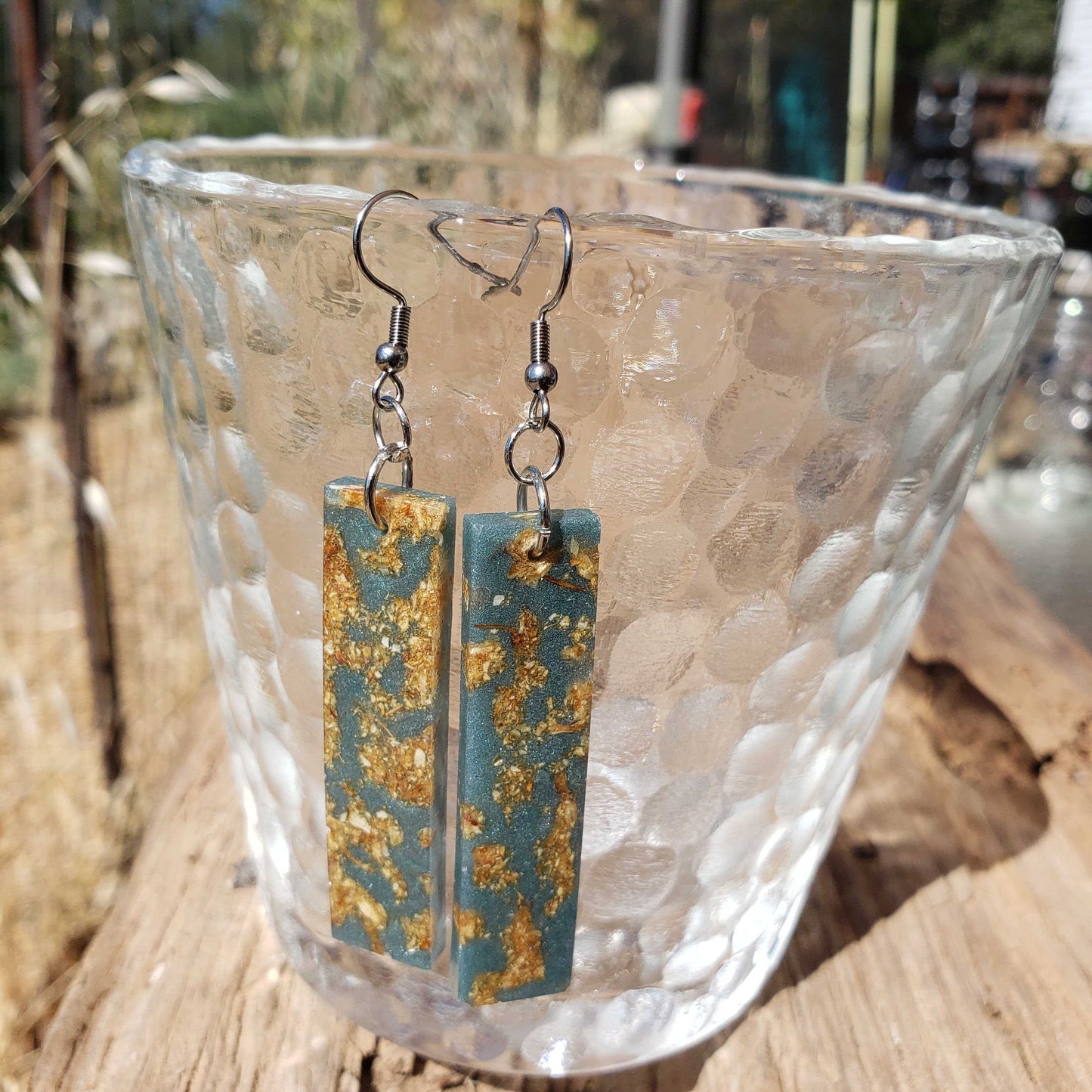 Teal and gold rectangular boho earrings with dried flowershanging from a glass bowl.