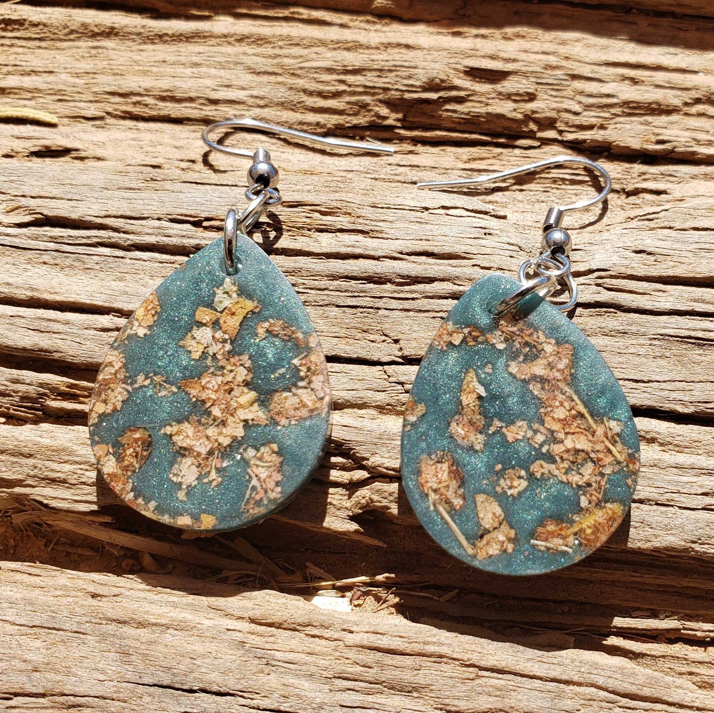 Teal earrings with gold leaf pattern made from dried leaves on a wooden surface