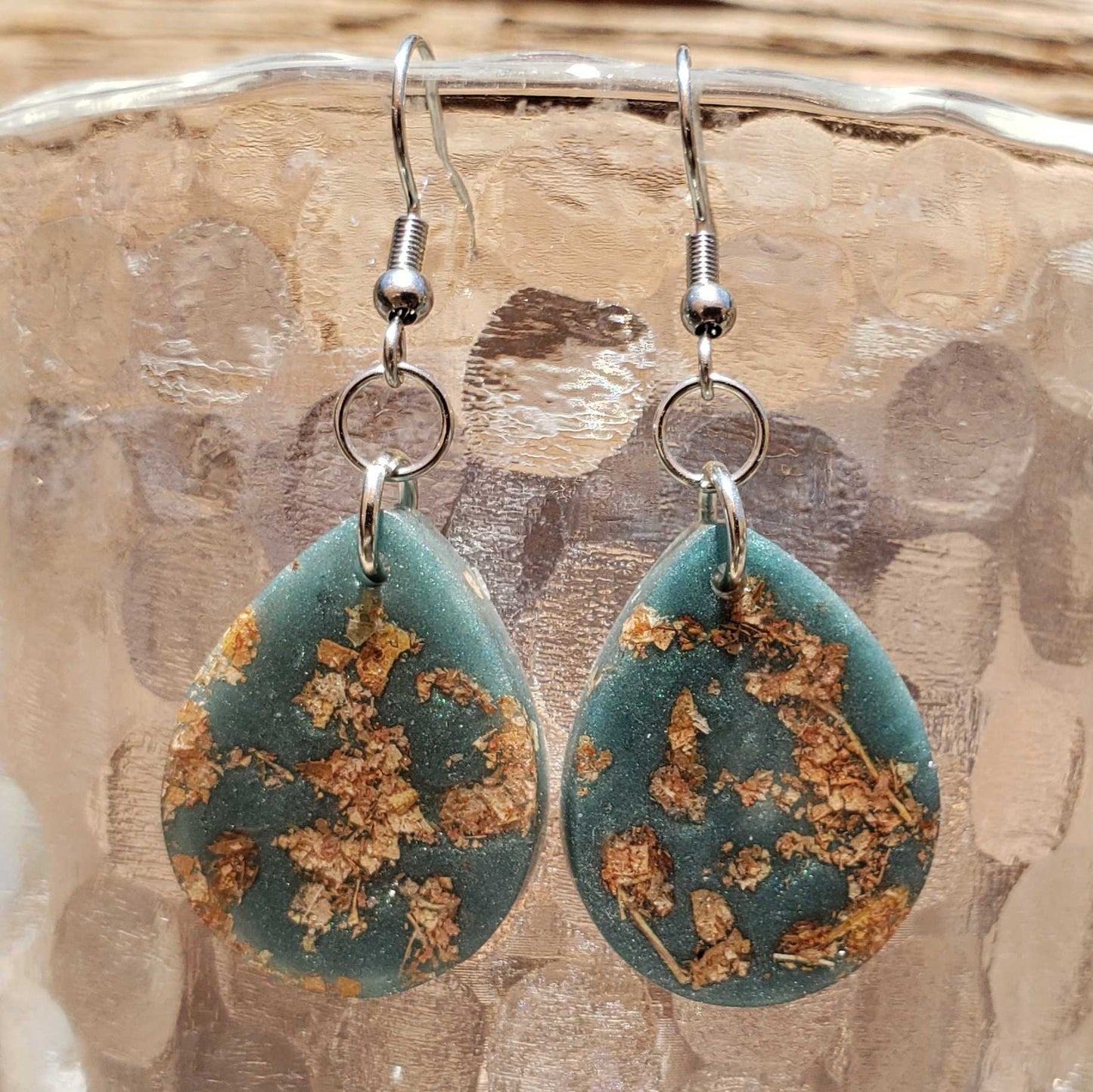 Teardrop-shaped boho earrings with floral design made from dried leaves on a textured surface