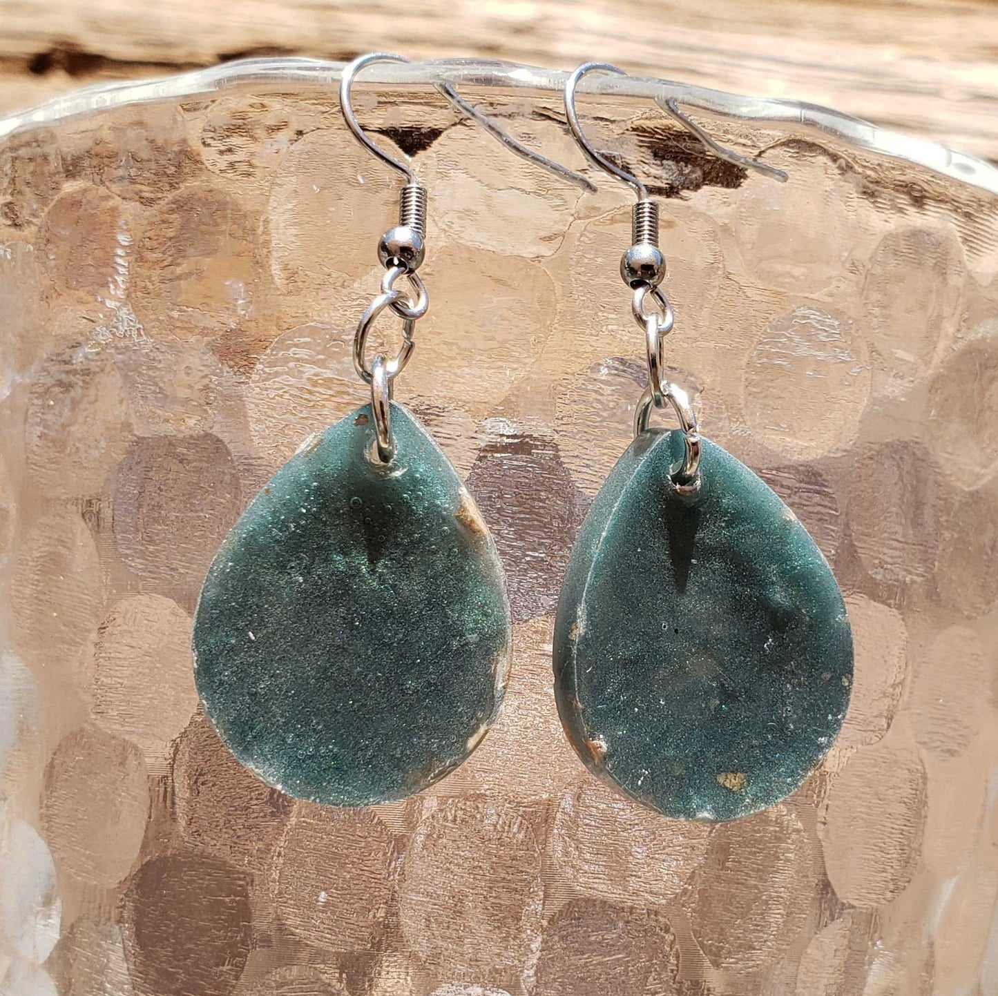 Backing of teal teardrop earrings on a textured beige surface