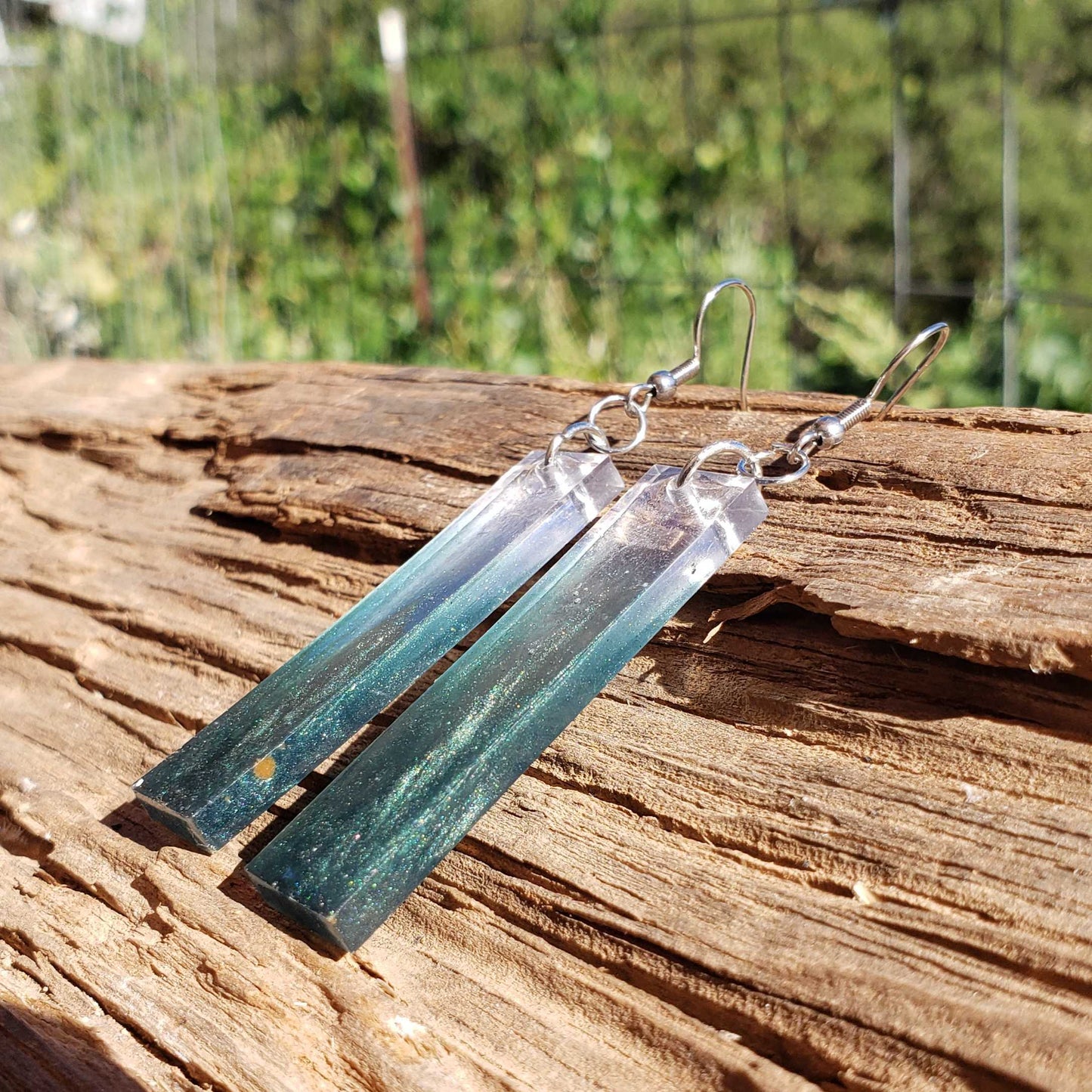 Teal and silver earrings on a wooden surface with a natural background