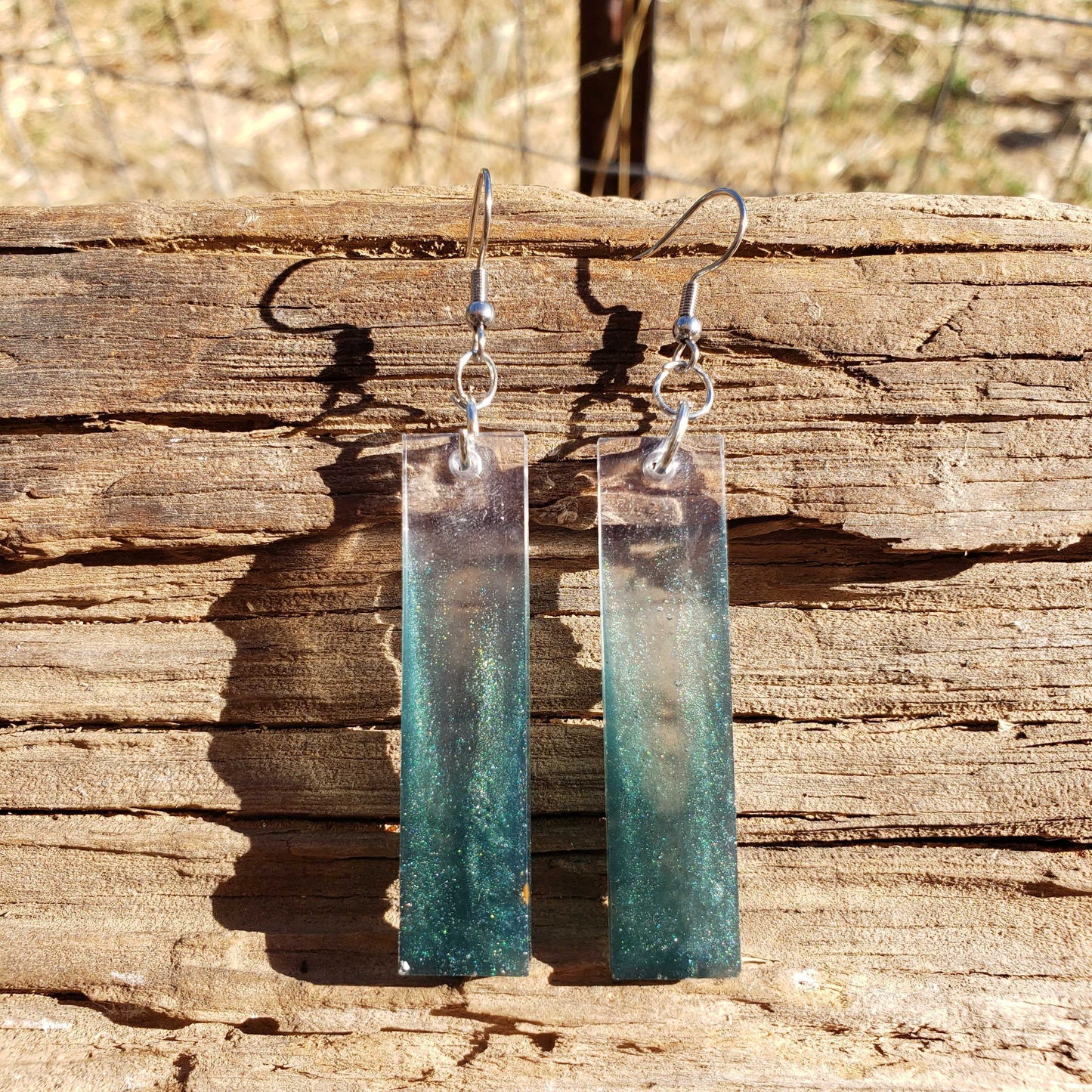 Teal and silver earrings hanging on a wooden surface