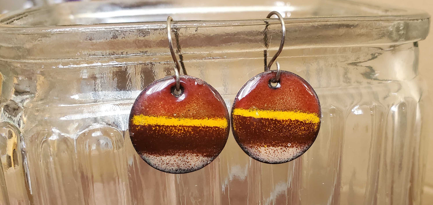 Round copper earrings with brown and yellow design on a glass jar