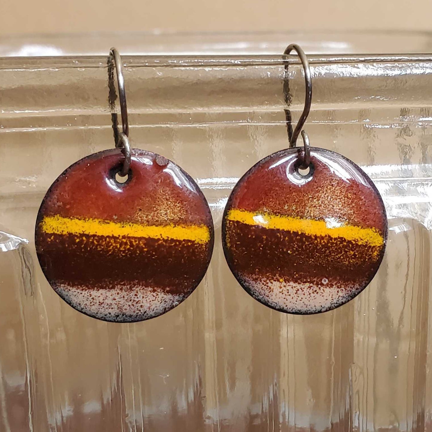 Round copper earrings with a yellow stripe on a glass jar