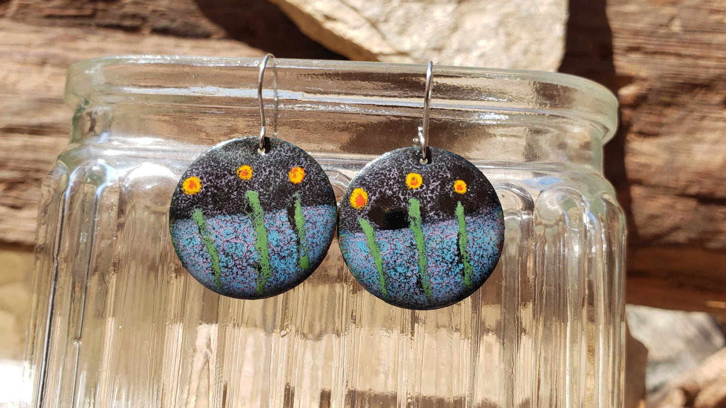 Pair of copper earrings with flower-themed design on a glass jar against a wooden background