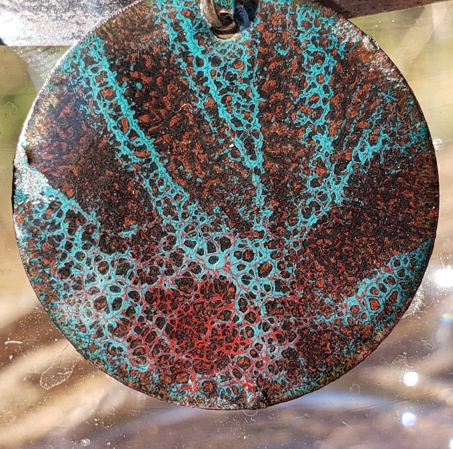 Round copper enamel earring with a unique, multicolored pattern on a reflective surface
