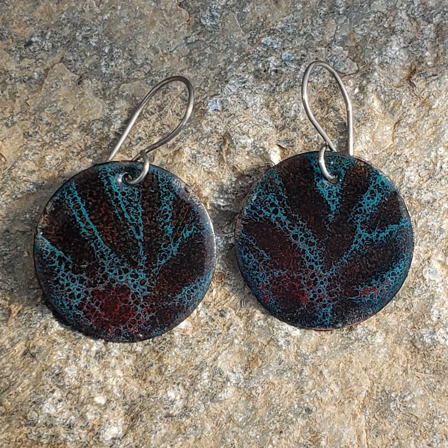Pair of round copper enamel boho earrings with a marbled design on a stone surface
