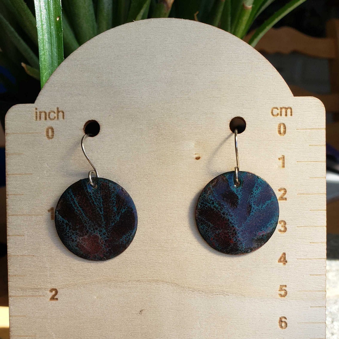 Pair of round copper earrings on a wooden display card with measurements, against a natural background.
