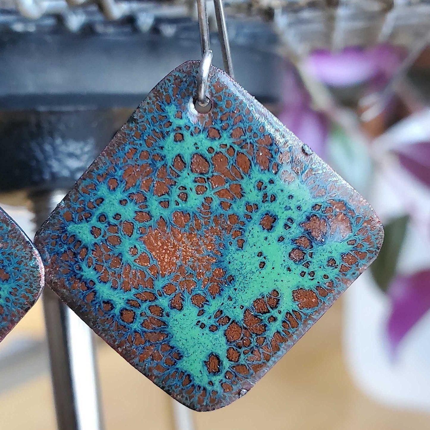 Square copper enamel earrings with blue and brown pattern on a blurred background