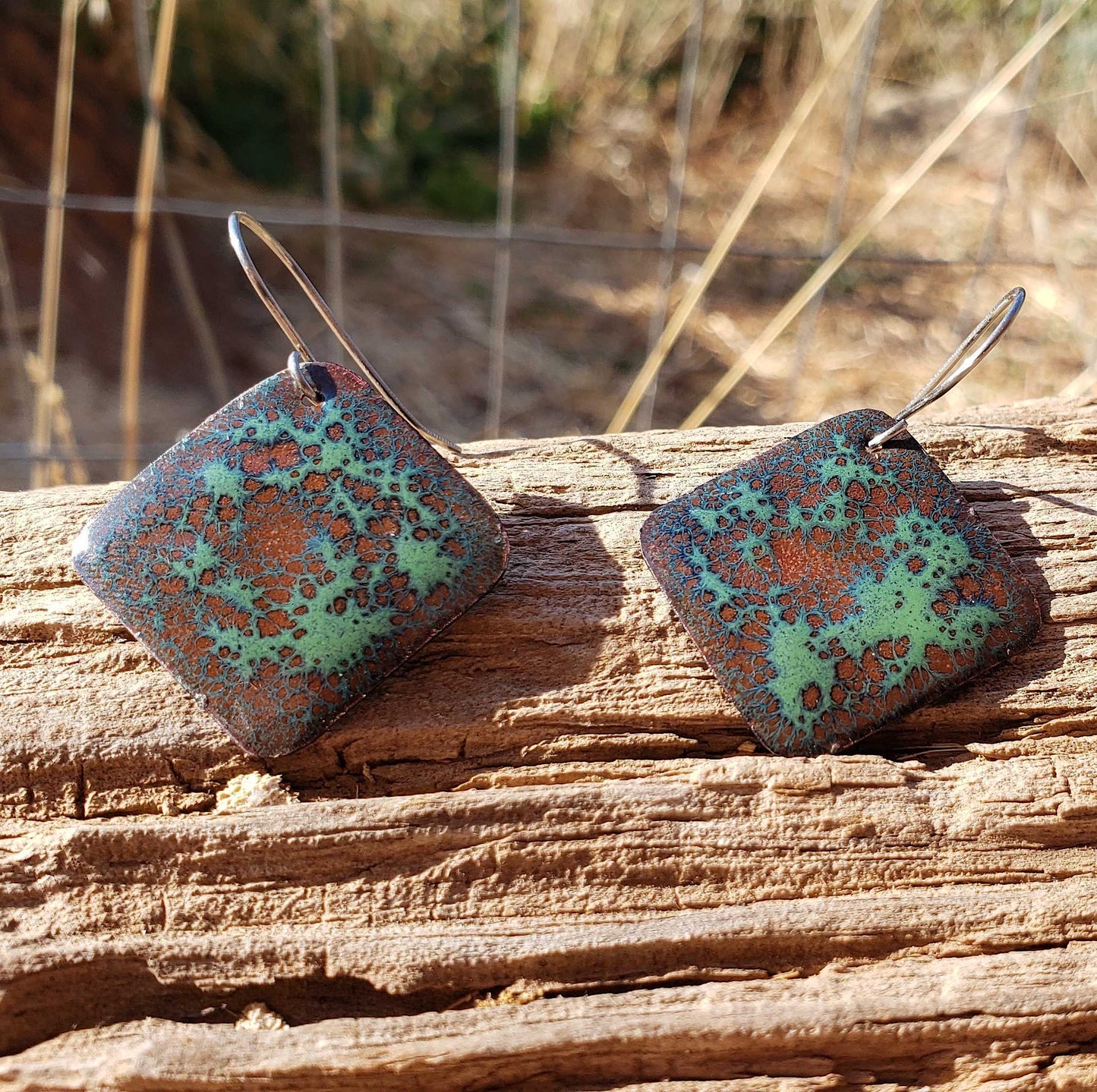 Square copper enamel earrings with a green and brown pattern on a wooden surface
