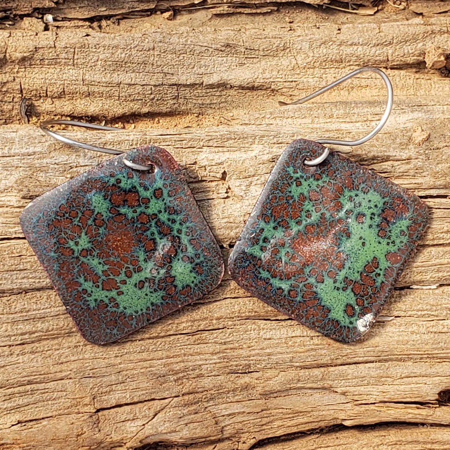 Pair of copper enamel boho square earrings with a pattern on a wooden surface