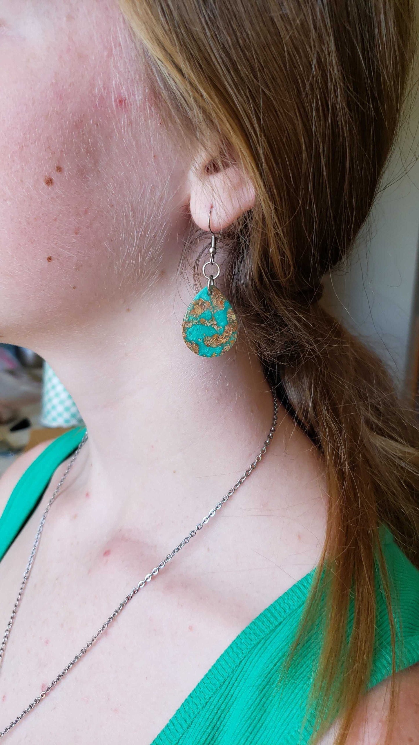 Close-up of a person wearing a green and gold earring made from dried leaves.