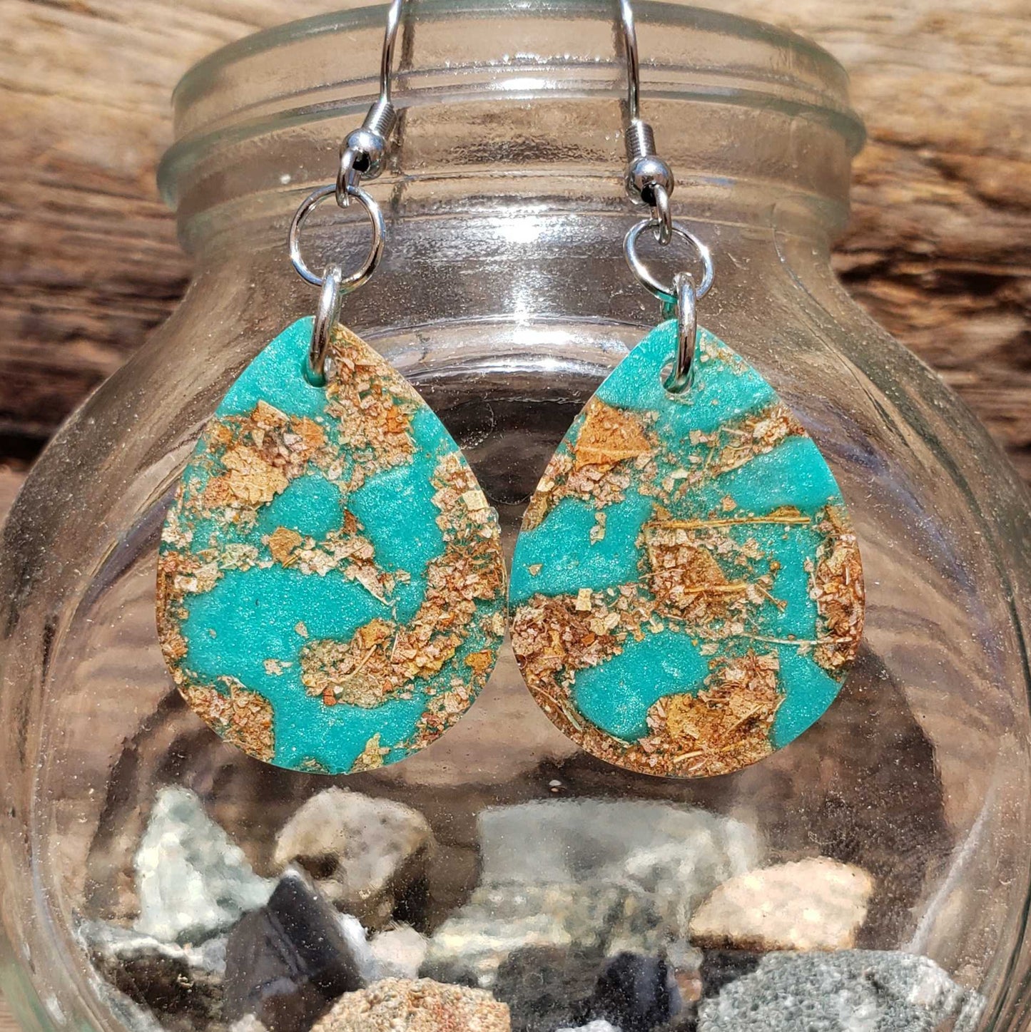 Boho turquoise and gold teardrop earrings made from dried leaves on a glass jar with stones
