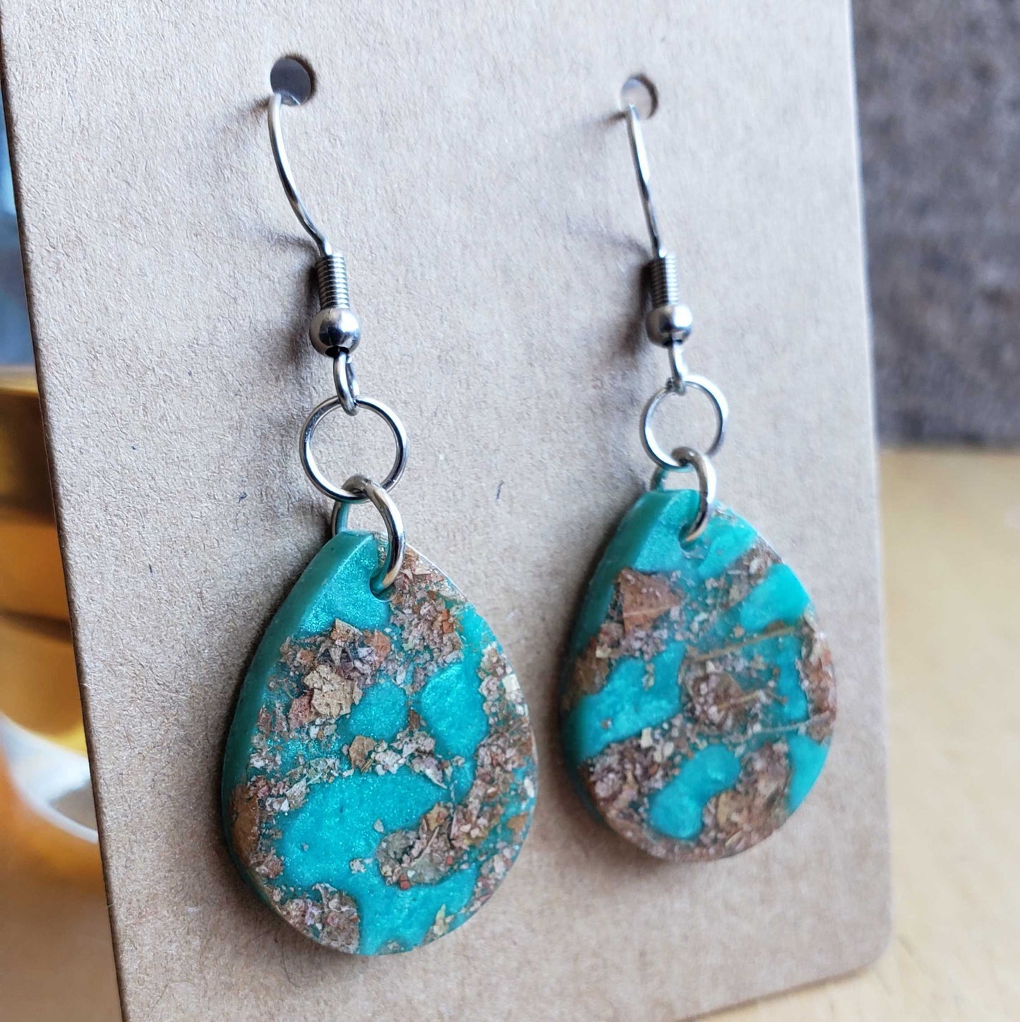 Boho turquoise teardrop made from dried leaves earrings on a display card with a blurred background