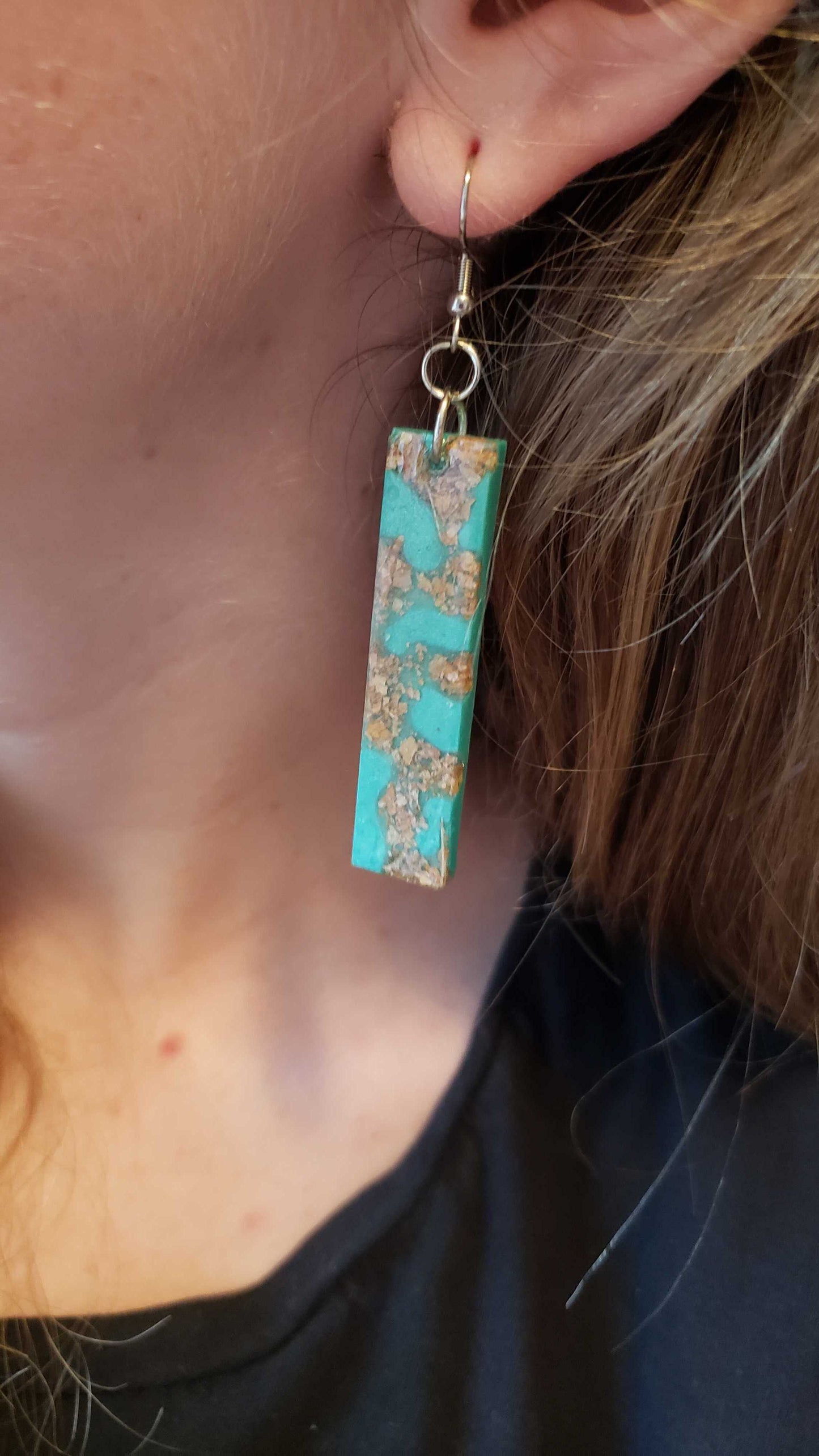 Turquoise rectangular earring with floral pattern made with dried leaves worn by a person