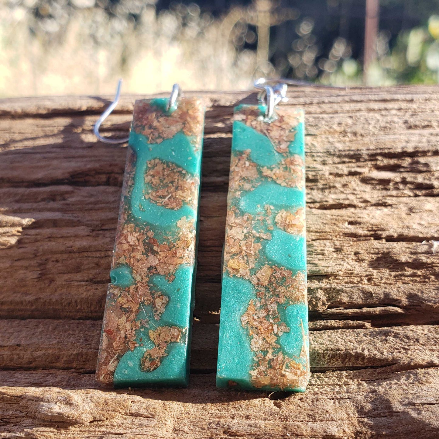 Turquoise and brown patterned earrings made from dried leaves on a wooden surface