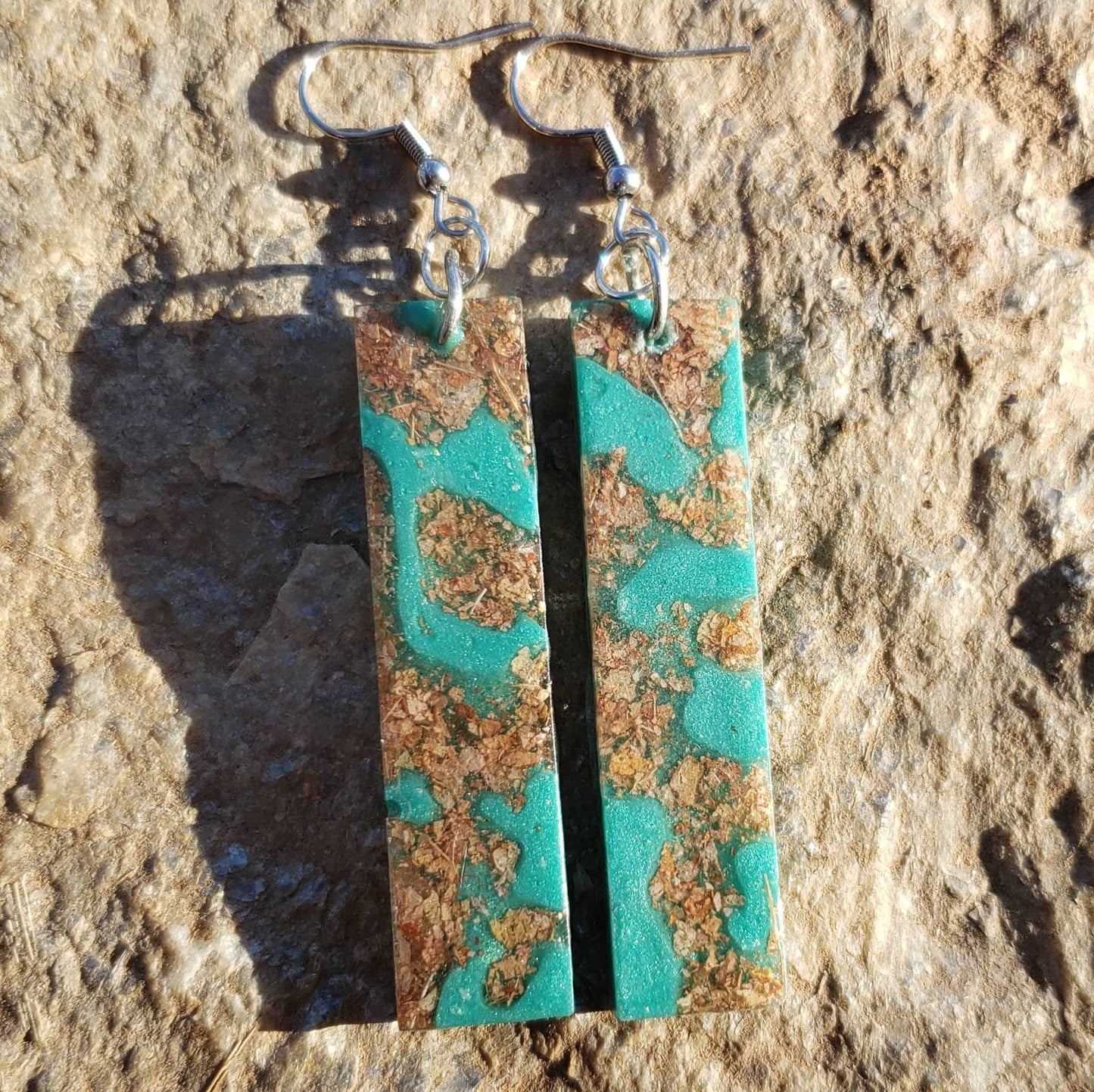 Turquoise and brown patterned earrings made with dried leaves on a stone surface