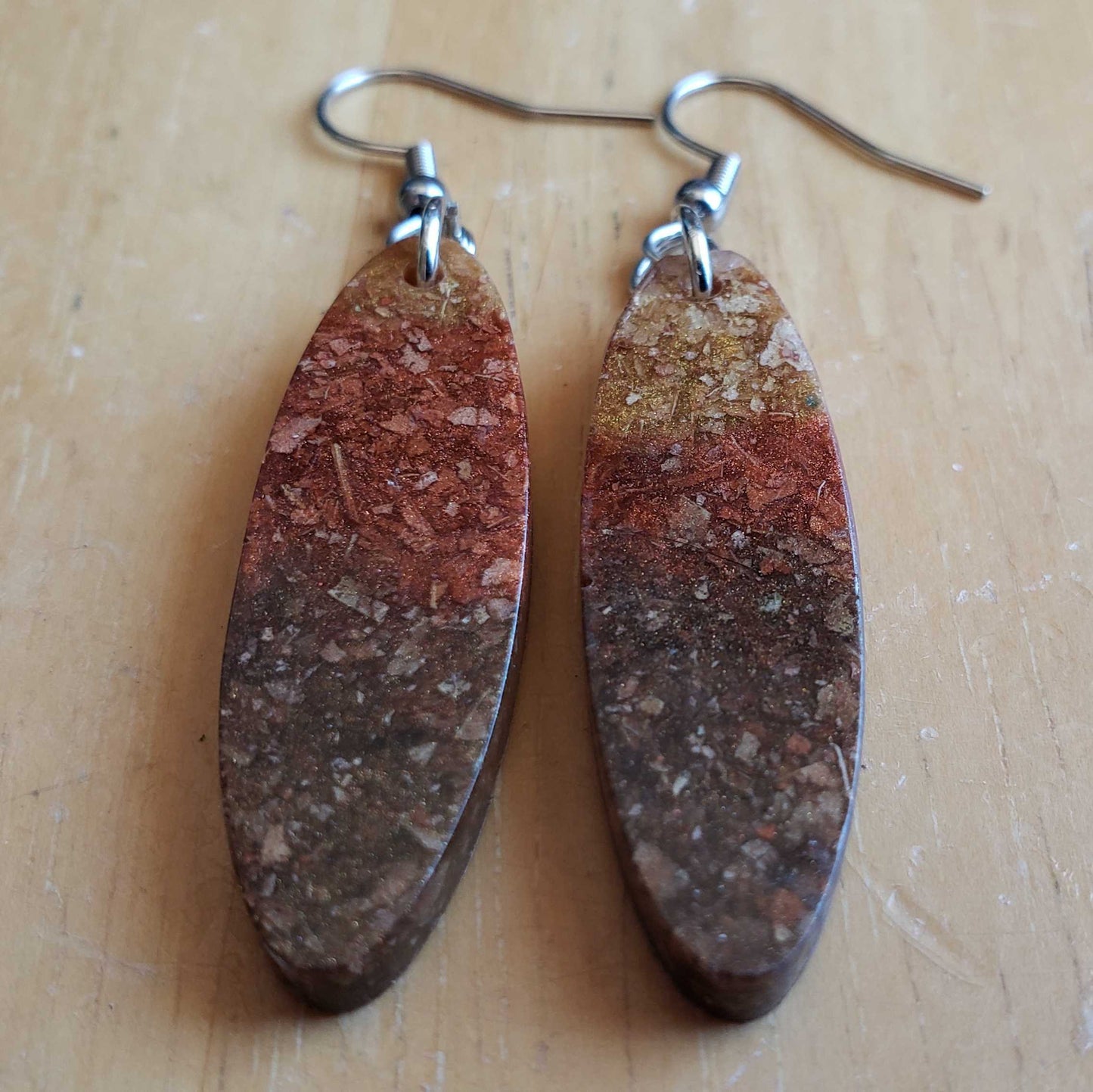 Pair of earrings with brown and red marbled design made from dried leaves on a beige surface