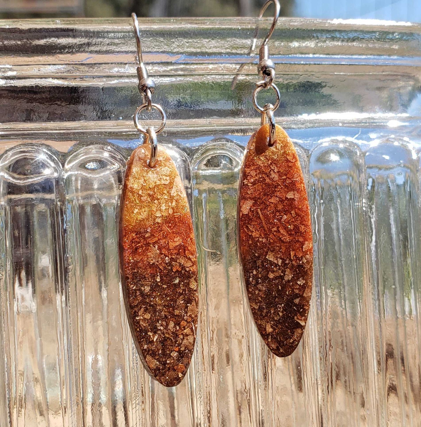 Brown oval earrings made from dried leaves on a clear glass surface