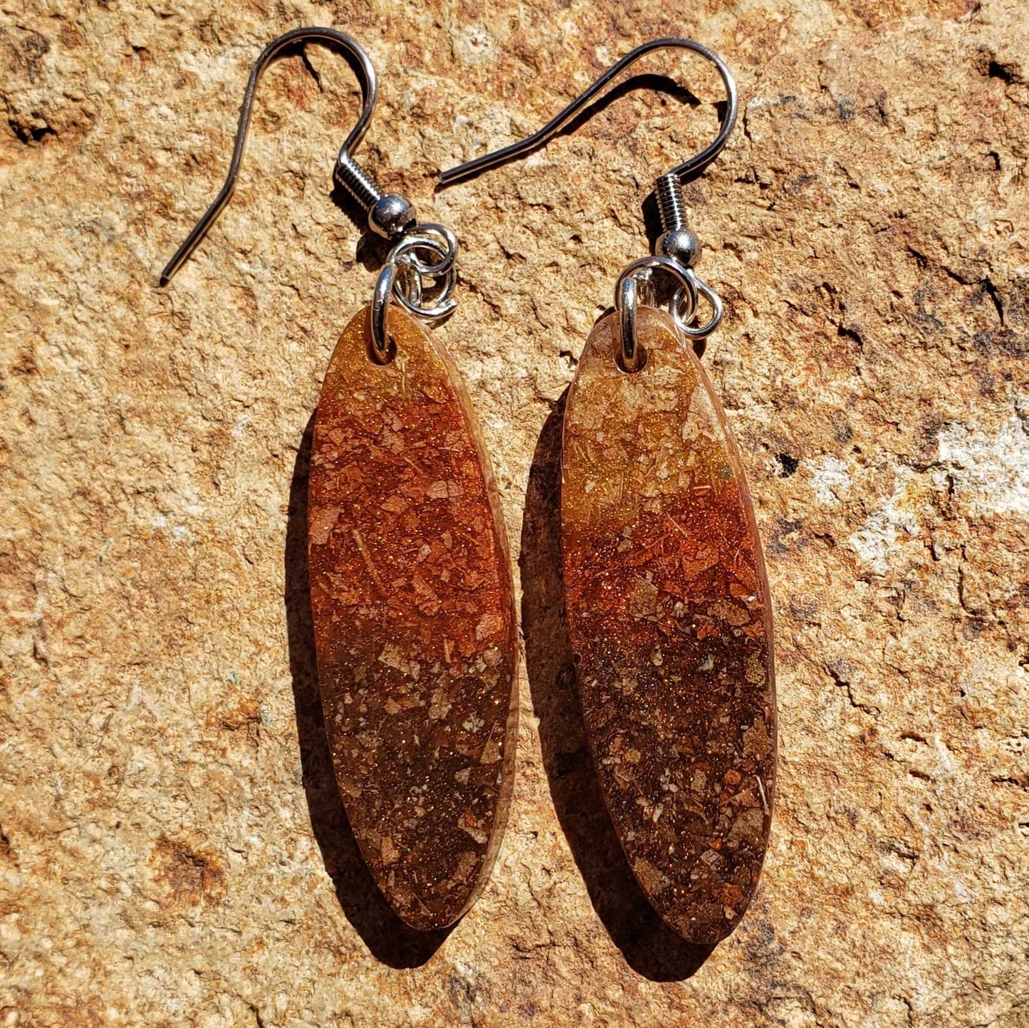 Pair of brown oval earrings made from dried leaves on a textured beige surface