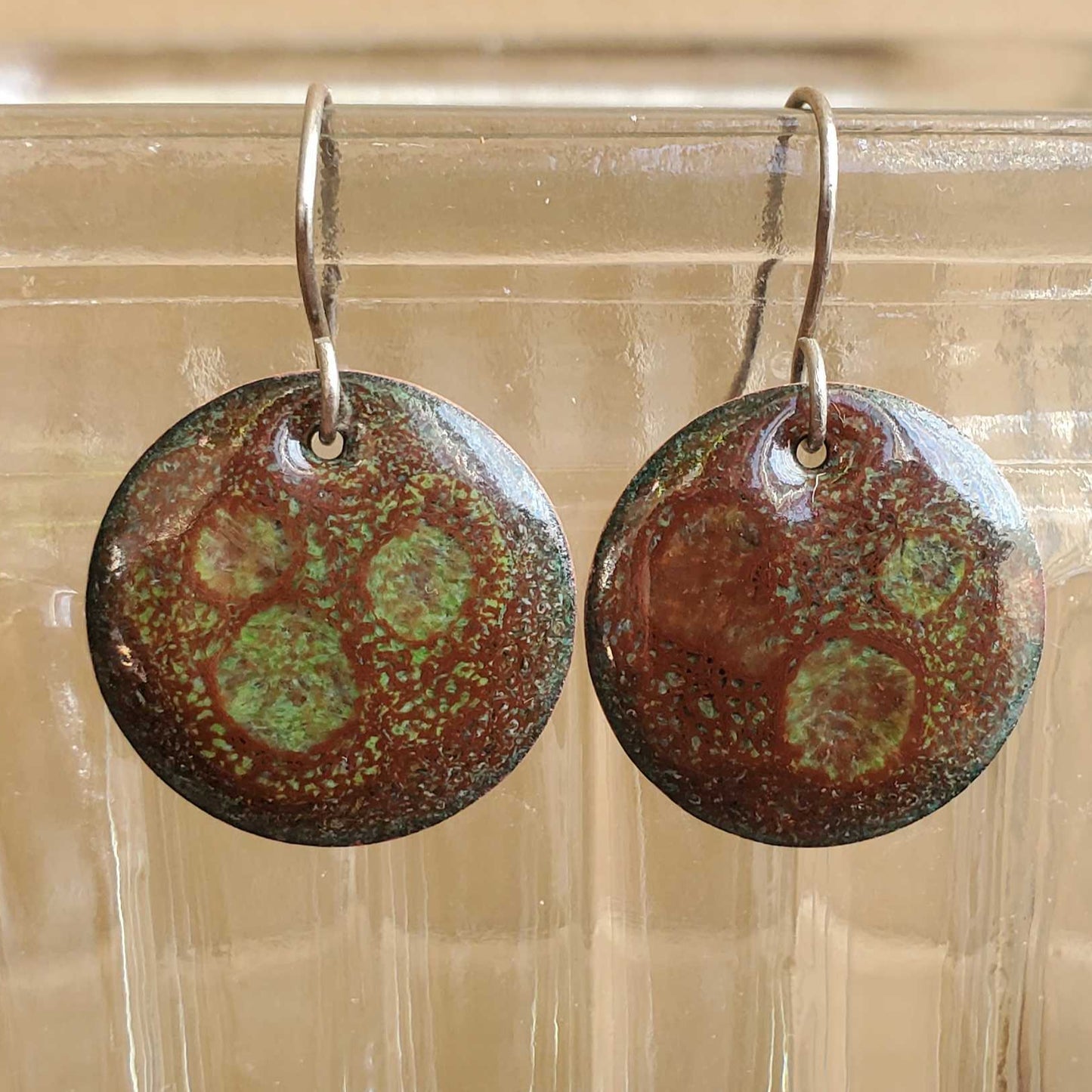 Pair of round copper and glass earrings with a pattern on a clear glass surface