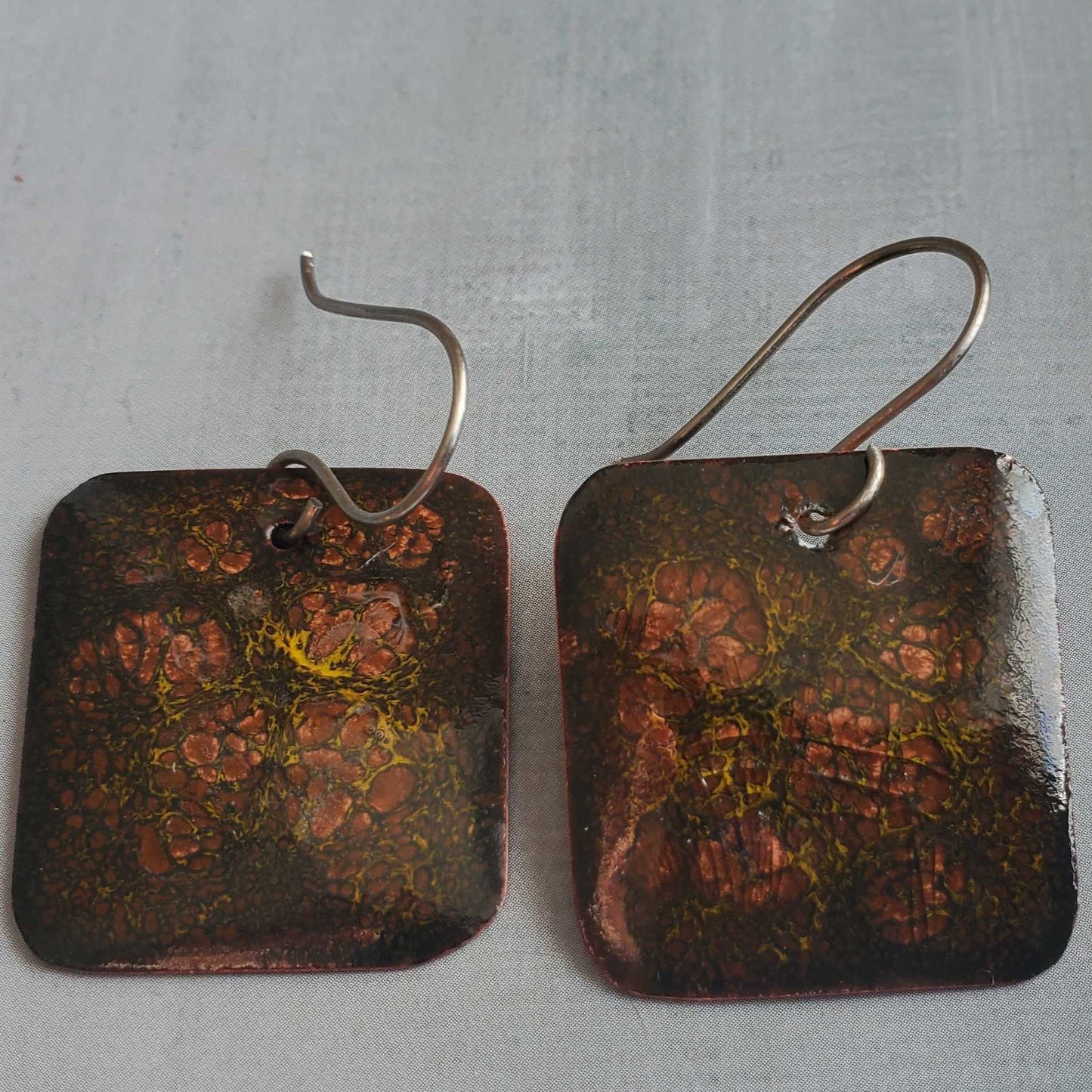 Pair of square copper earrings with crackle pattern on a gray background