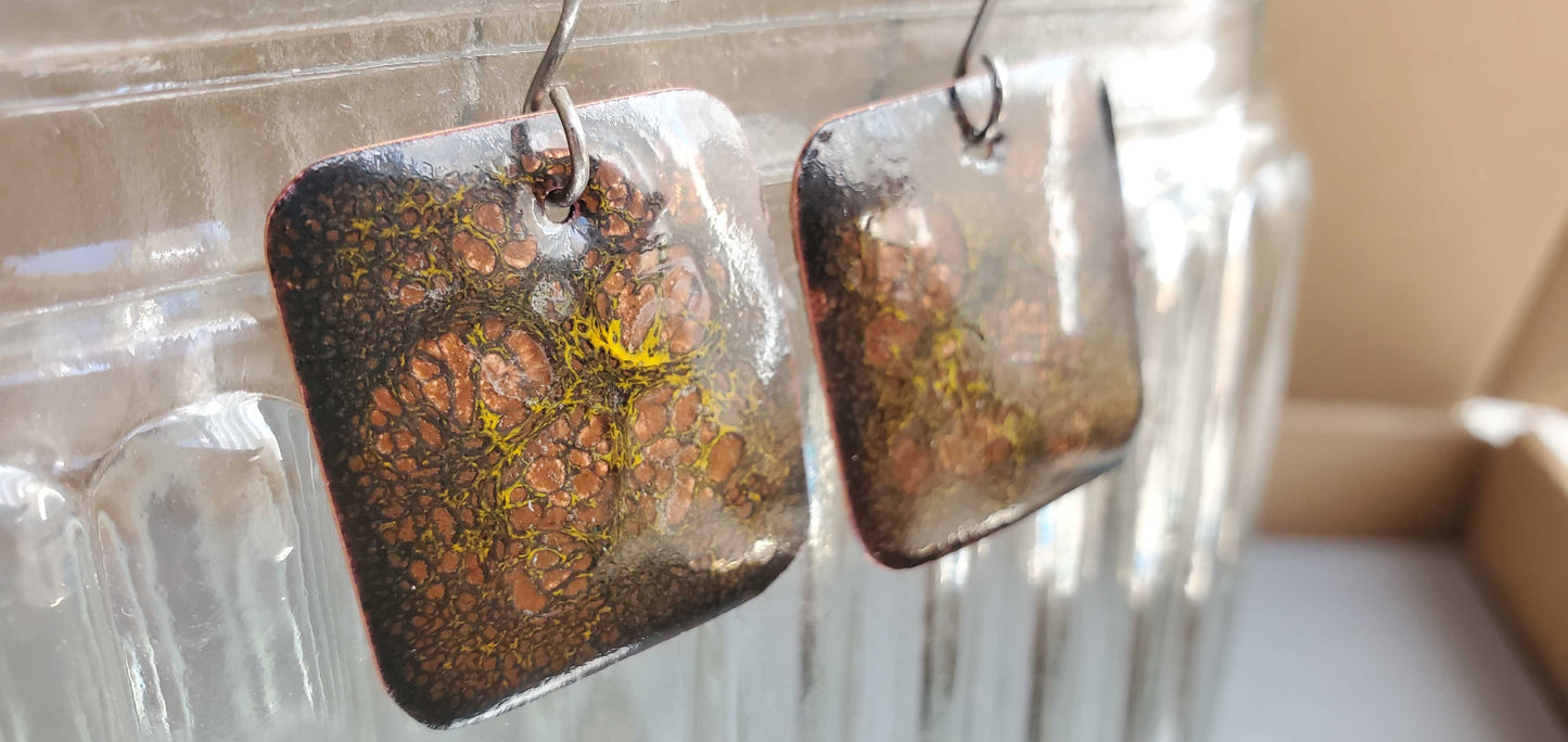 Pair of square copper earrings with a natural stone-like finish on a clear stand.