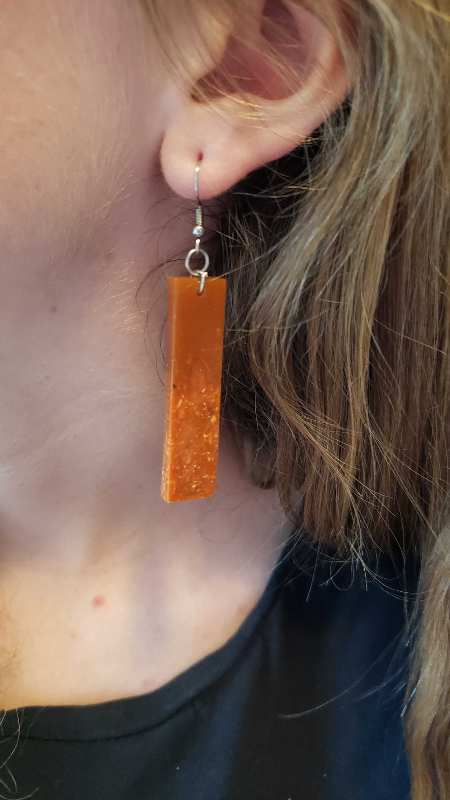 Close-up of a person wearing a rectangular orange earring made with dried jasmine flowers.