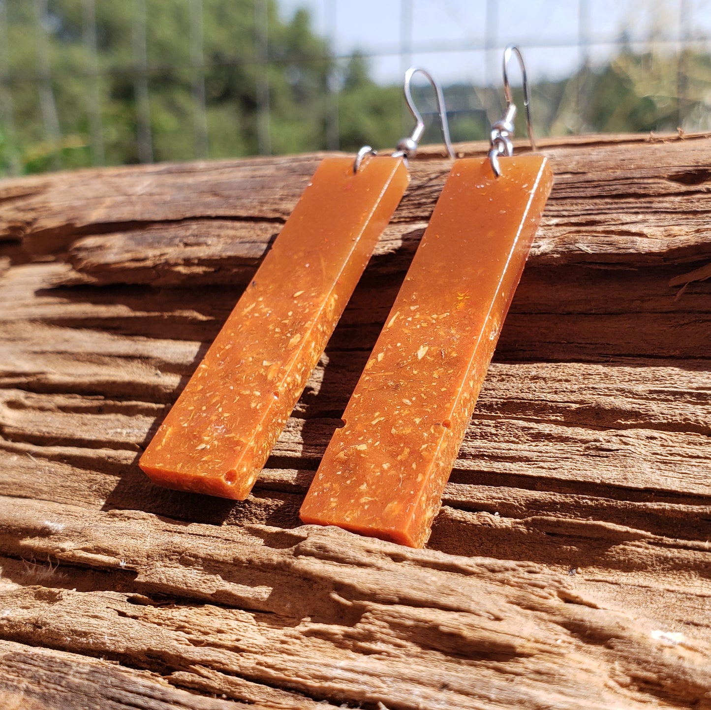 Amber colored bar-shaped earrings on a wooden surface with a natural background
