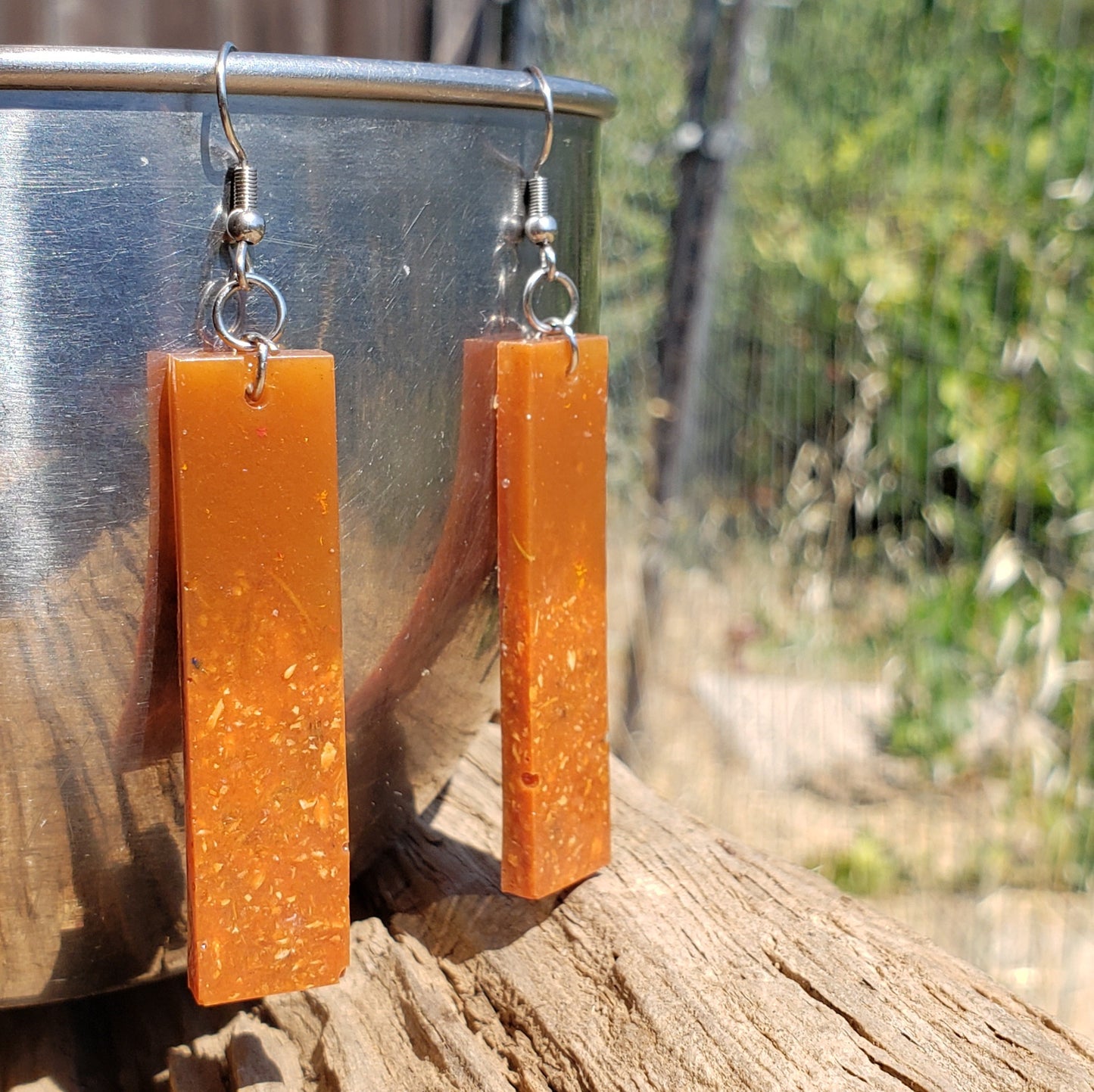 Orange bar-shaped earrings hanging on a metal surface with a natural background