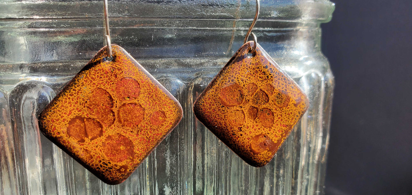 Square earrings with a textured orange-brown pattern hanging from a glass jar.