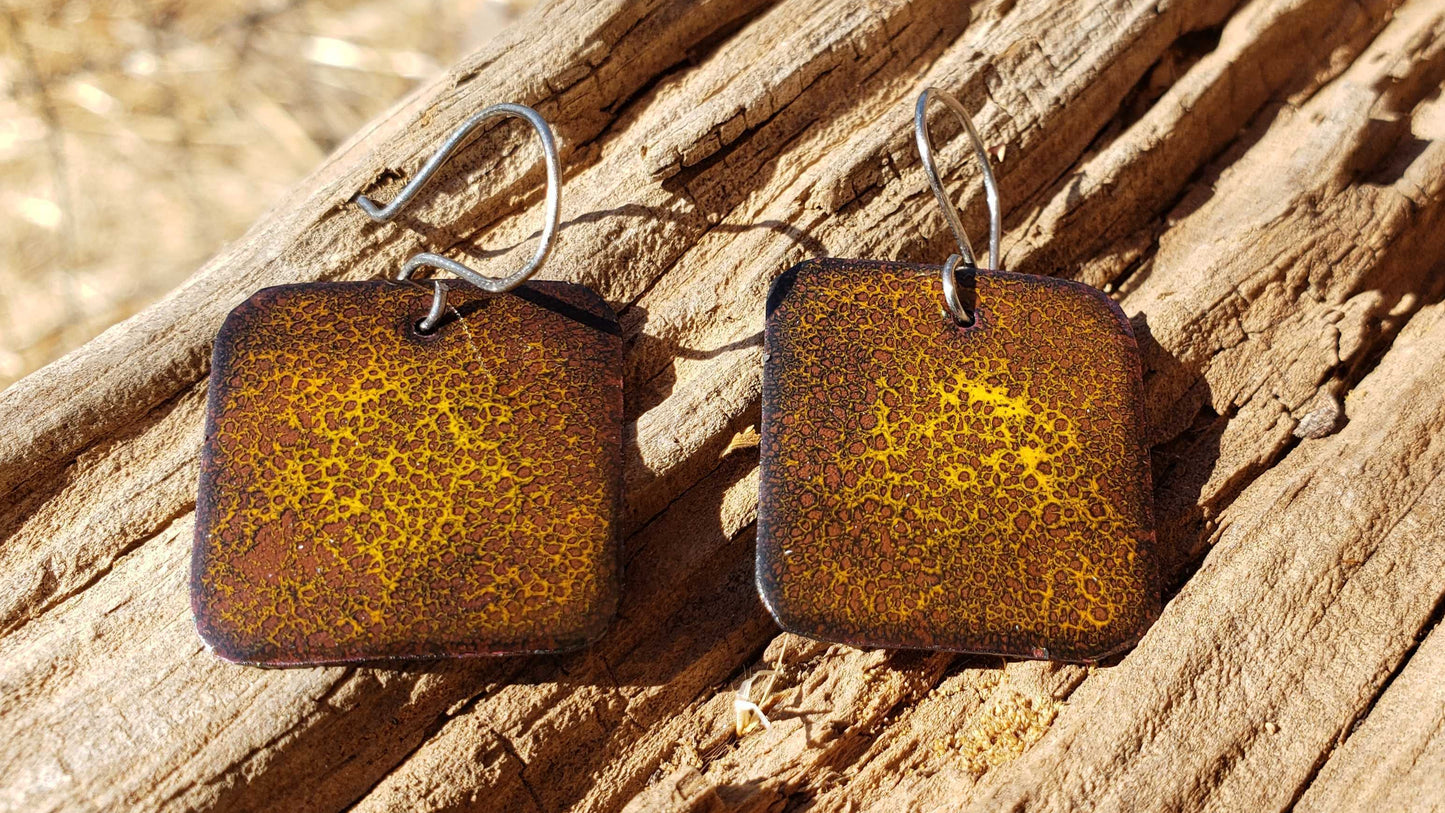 Brown square copper earrings earrings with a yellow pattern like a cheetah on a wooden surface