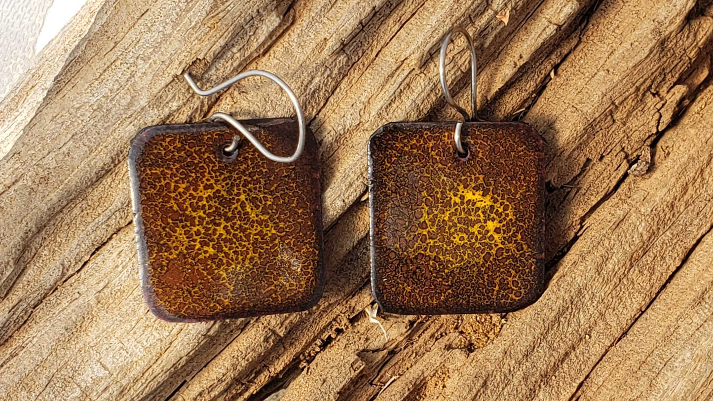 Pair of square brown copper boho dangle earrings with a yellow center on a wooden surface