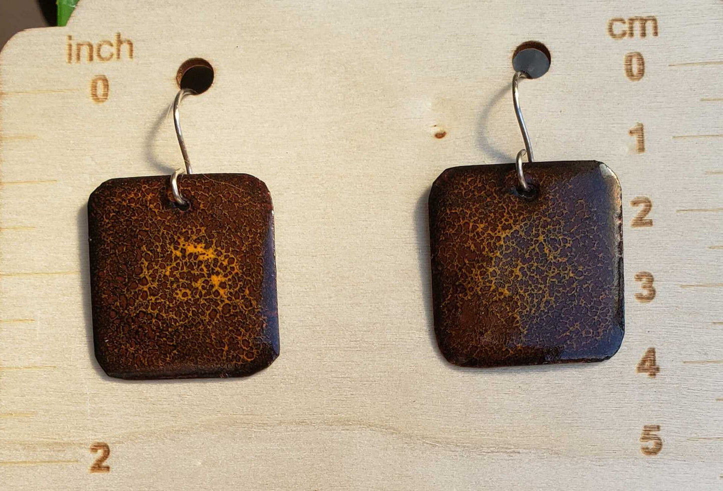 Pair of square rust-colored earrings on a wooden earring stand with measurements.