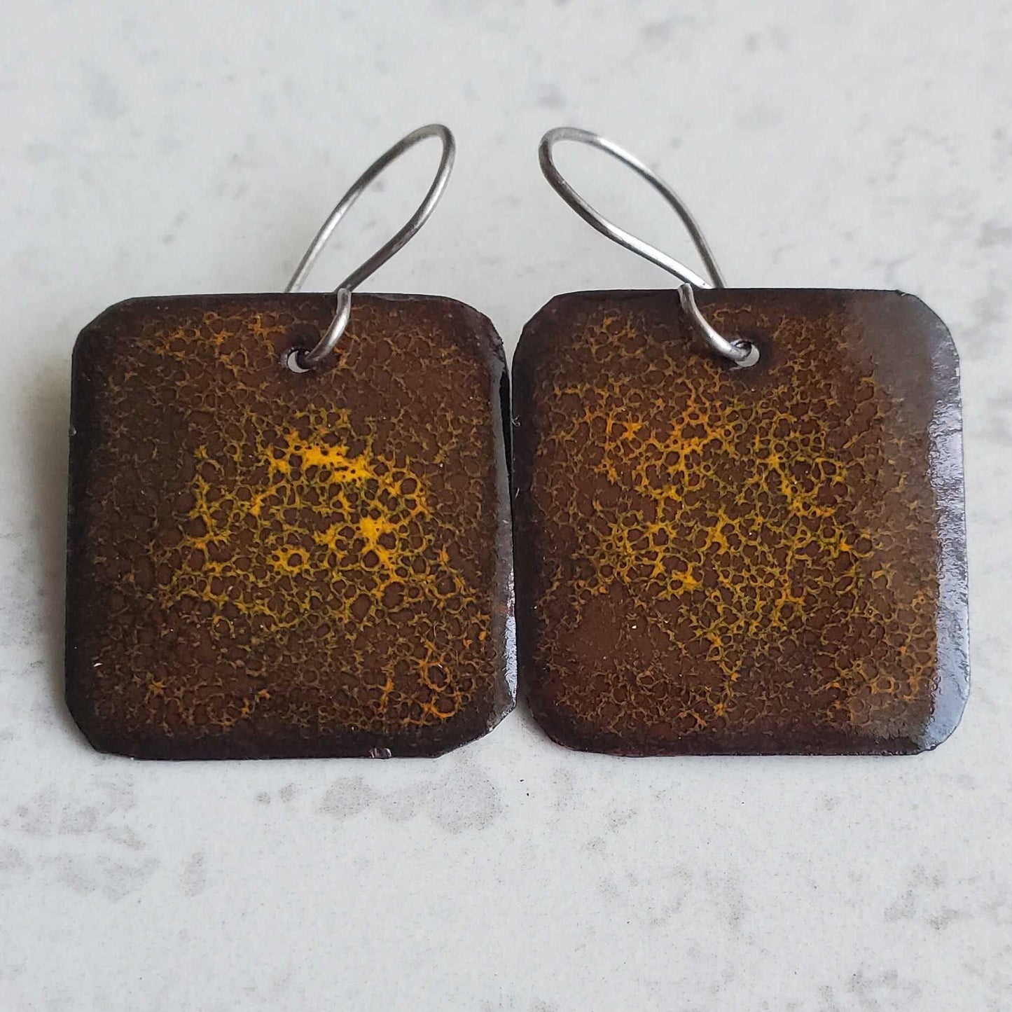 Pair of square earrings with brown and gold pattern on a light gray background