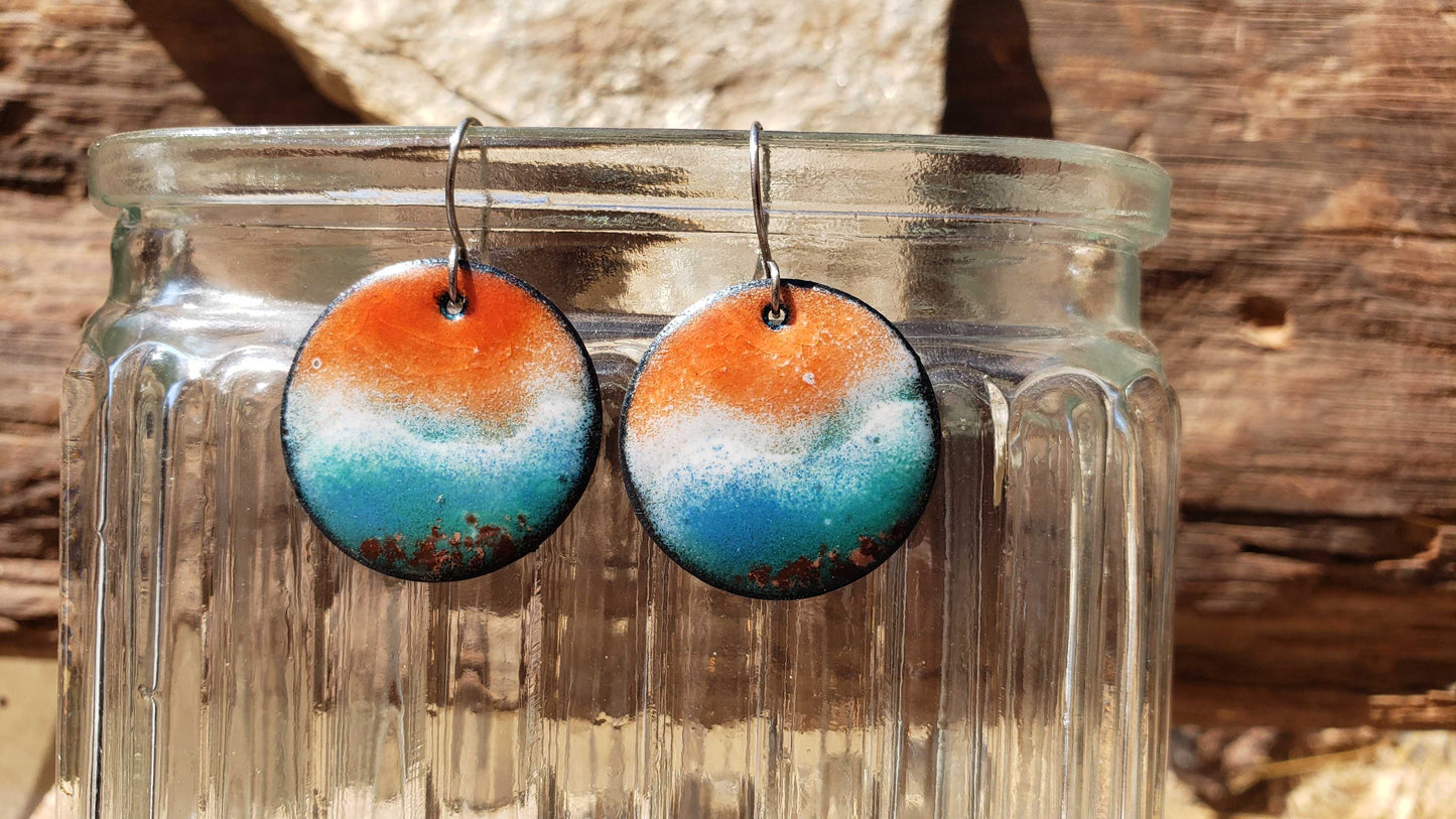 Round copper earrings with orange and blue gradient design inspired by the ocean in a clear glass jar