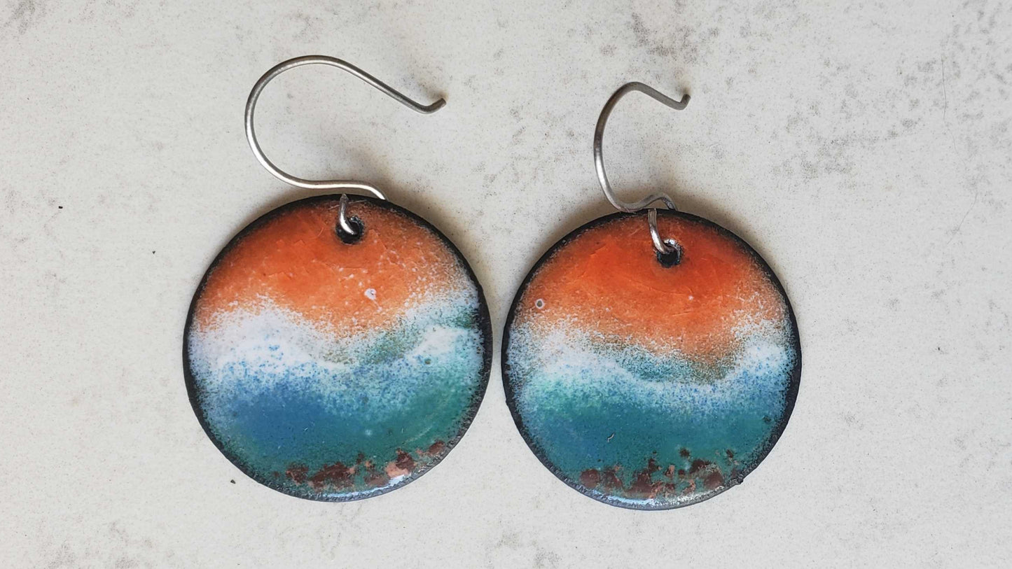 Pair of round copper earrings with a ocean scene and a gradient design on a light gray background