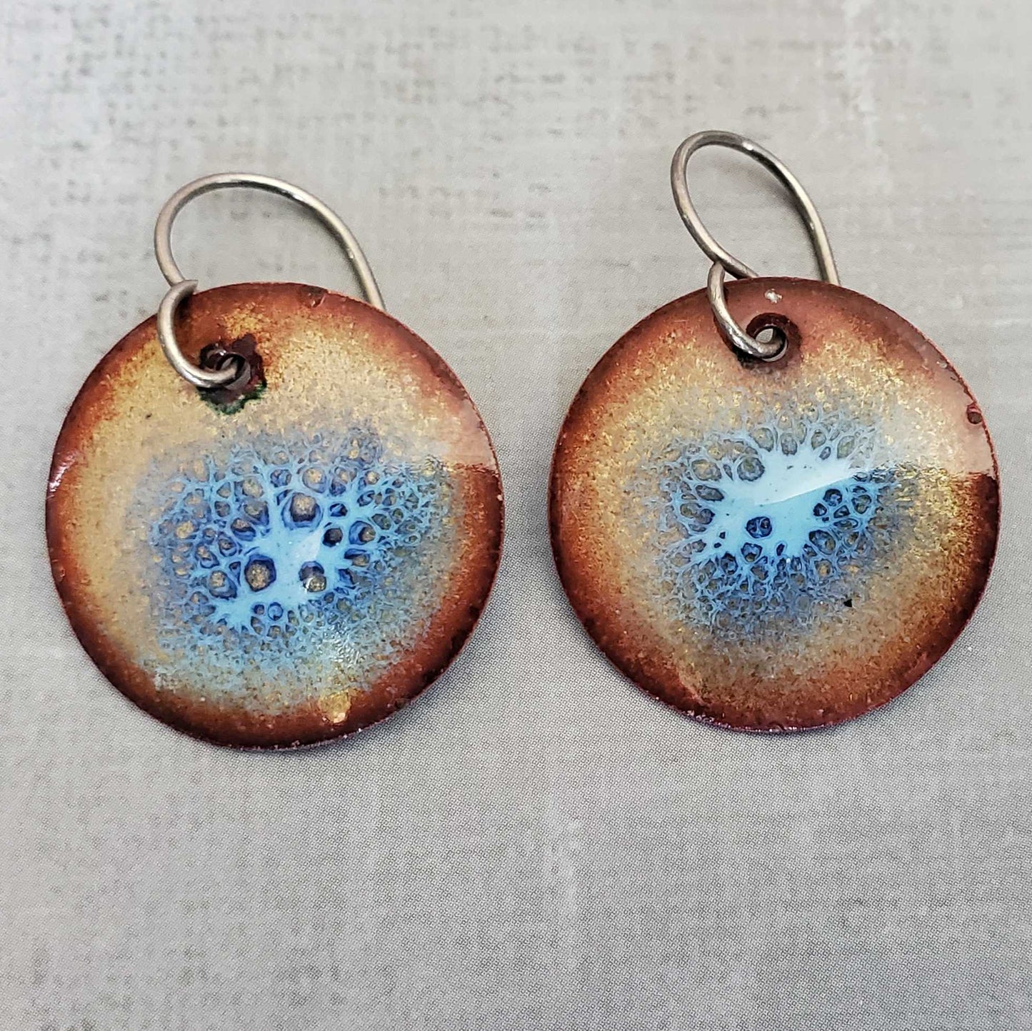 Pair of round copper earrings with blue and brown speckled design on a light gray background