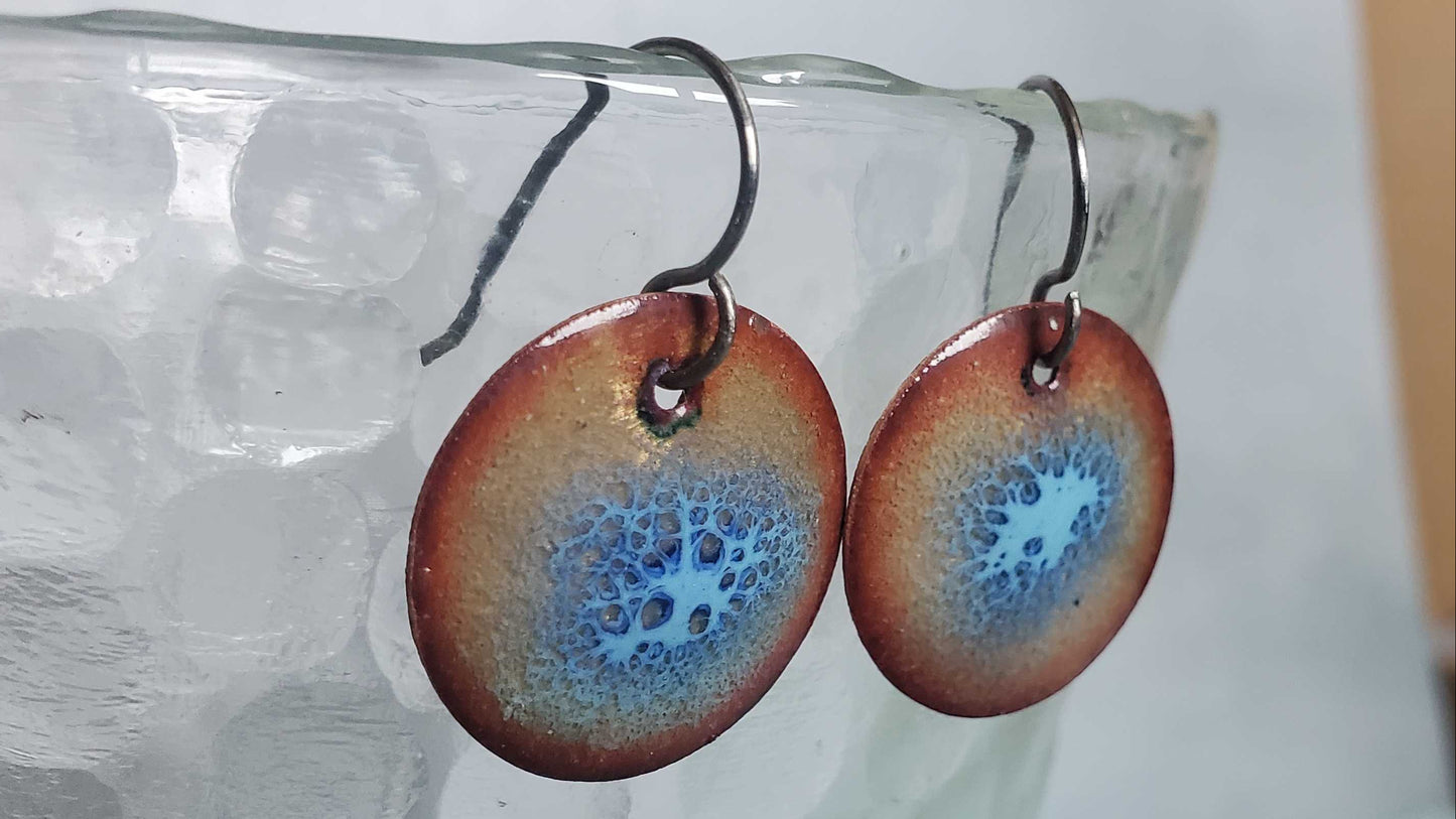 Copper enamel earrings with blue crackle design on a glass surface