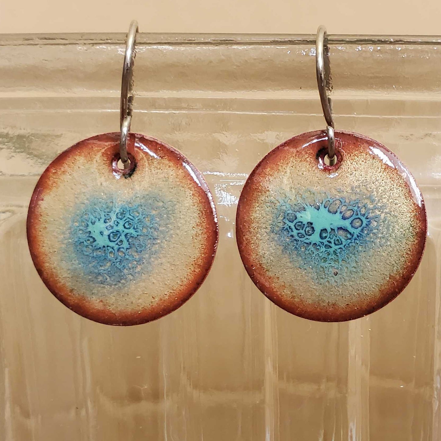 Round turquoise copper earrings with blue and brown design hanging from a glass jar.