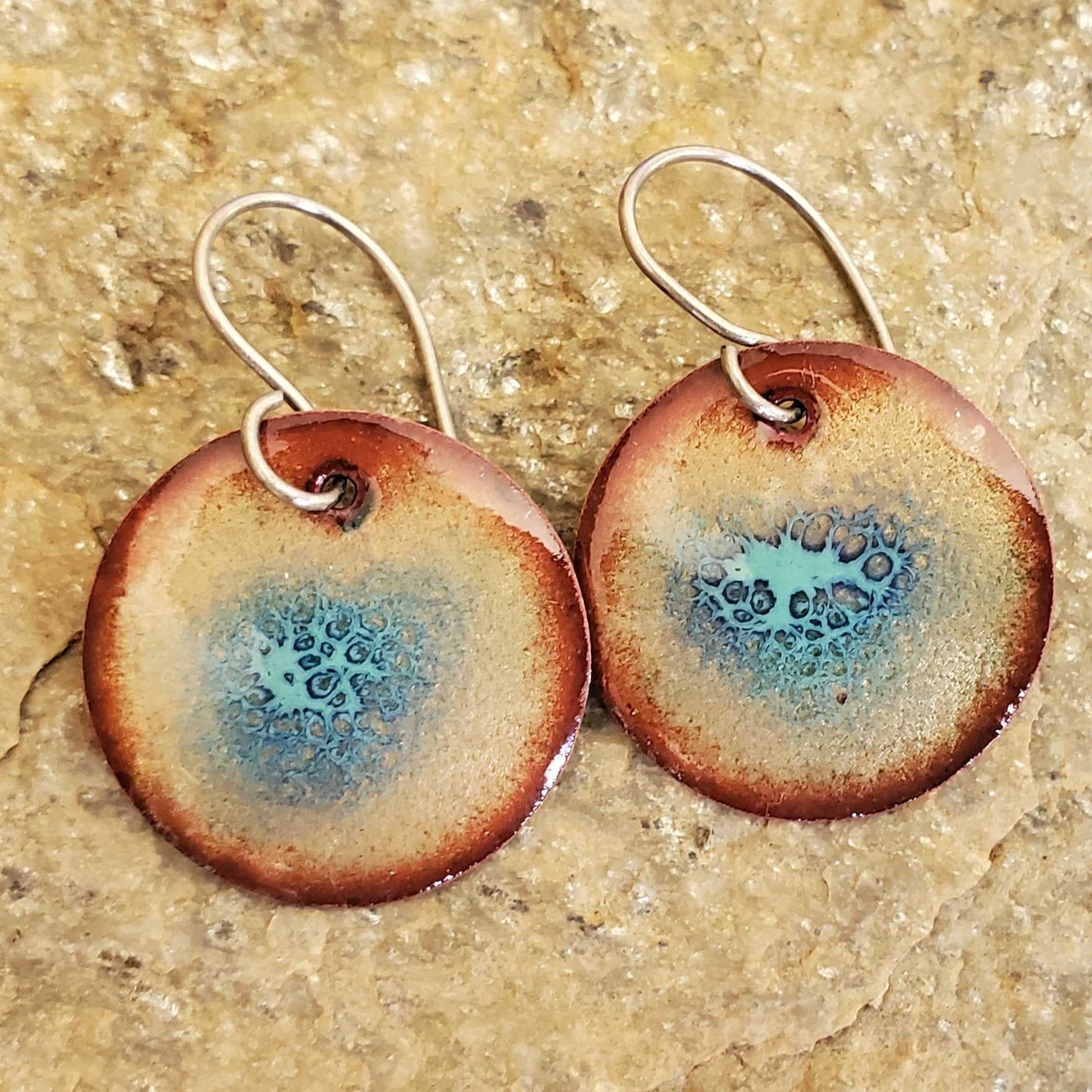 Pair of copper enamel earrings with blue interior on a textured beige surface