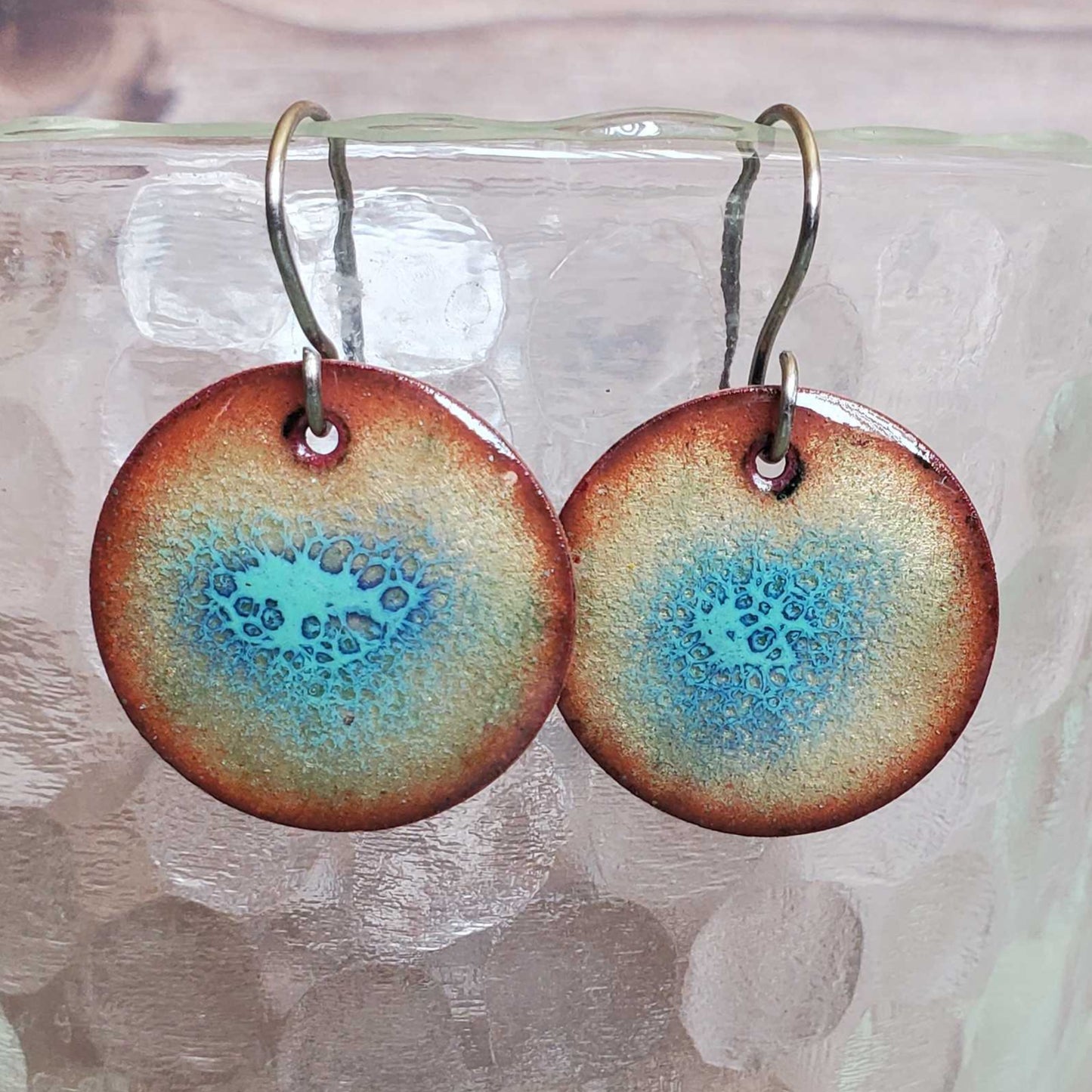 Round copper earrings with blue and copper design on a glass container