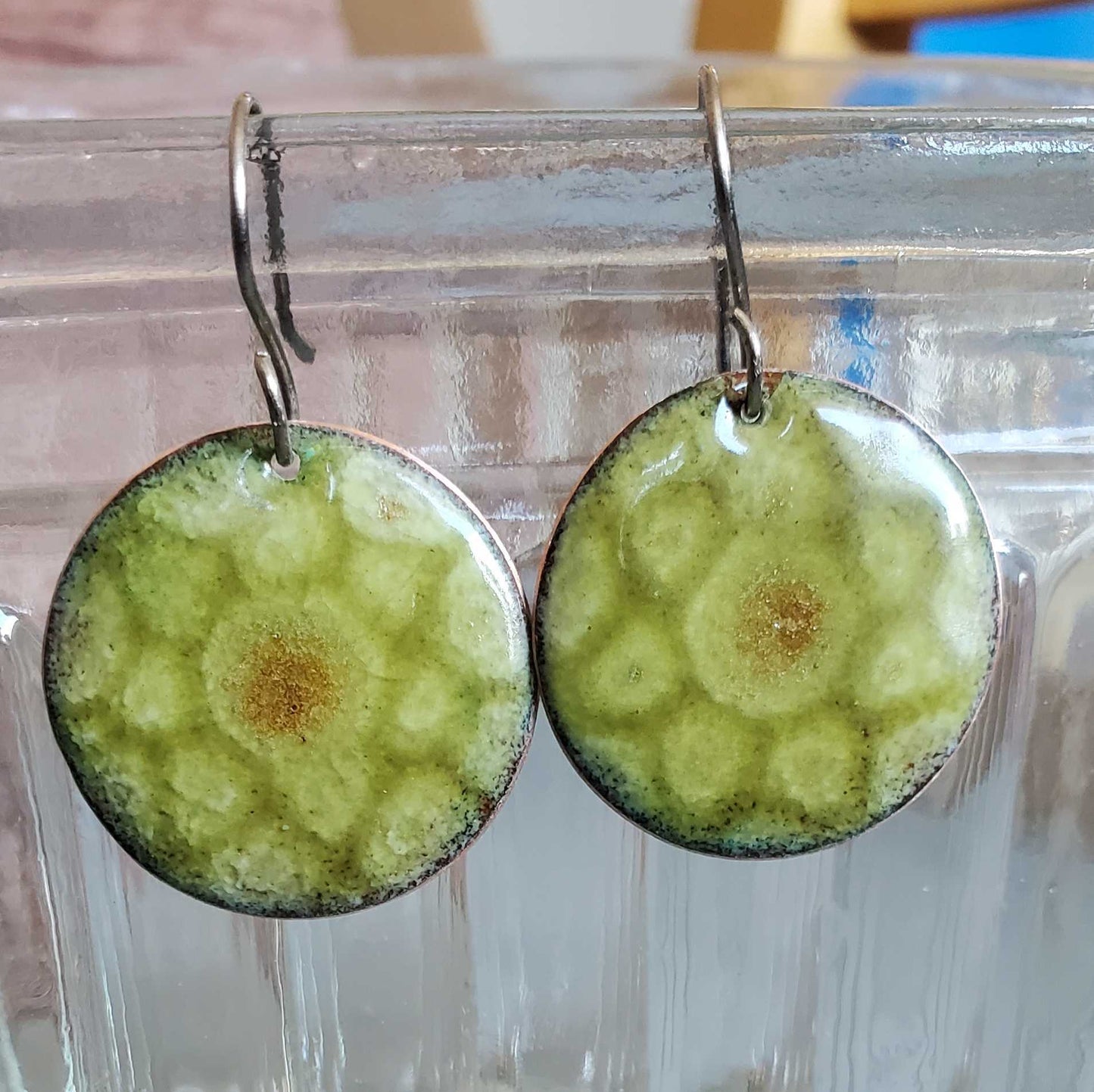 Green circular copper earrings with a brown center on a clear stand.